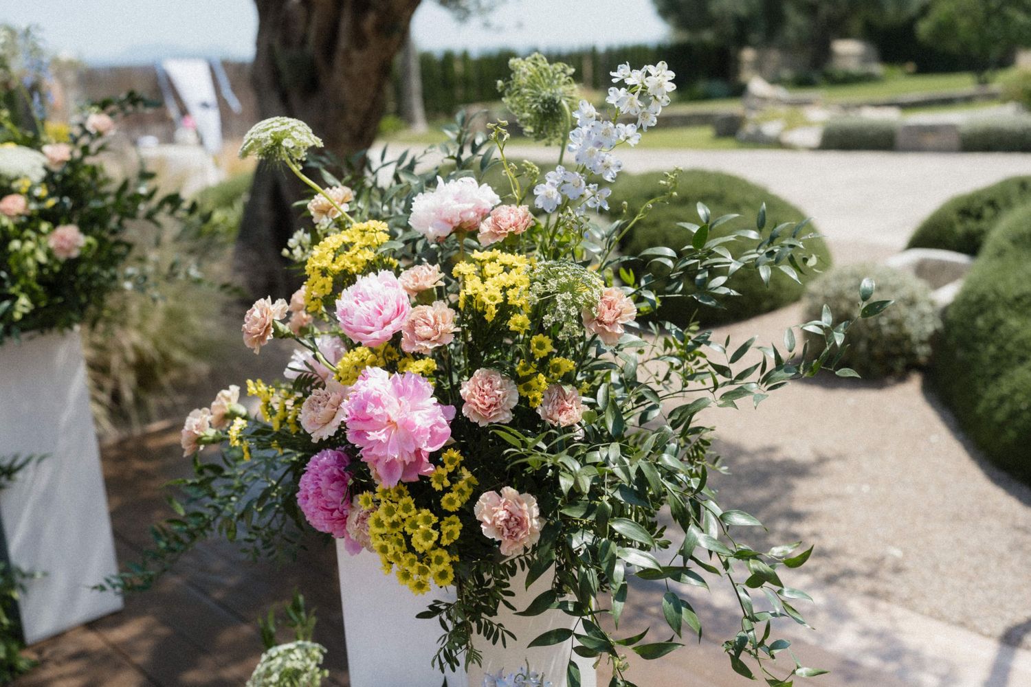 Elegant outdoor floral arrangement with pink peonies, yellow flowers, and greenery at a garden wedding ceremony.