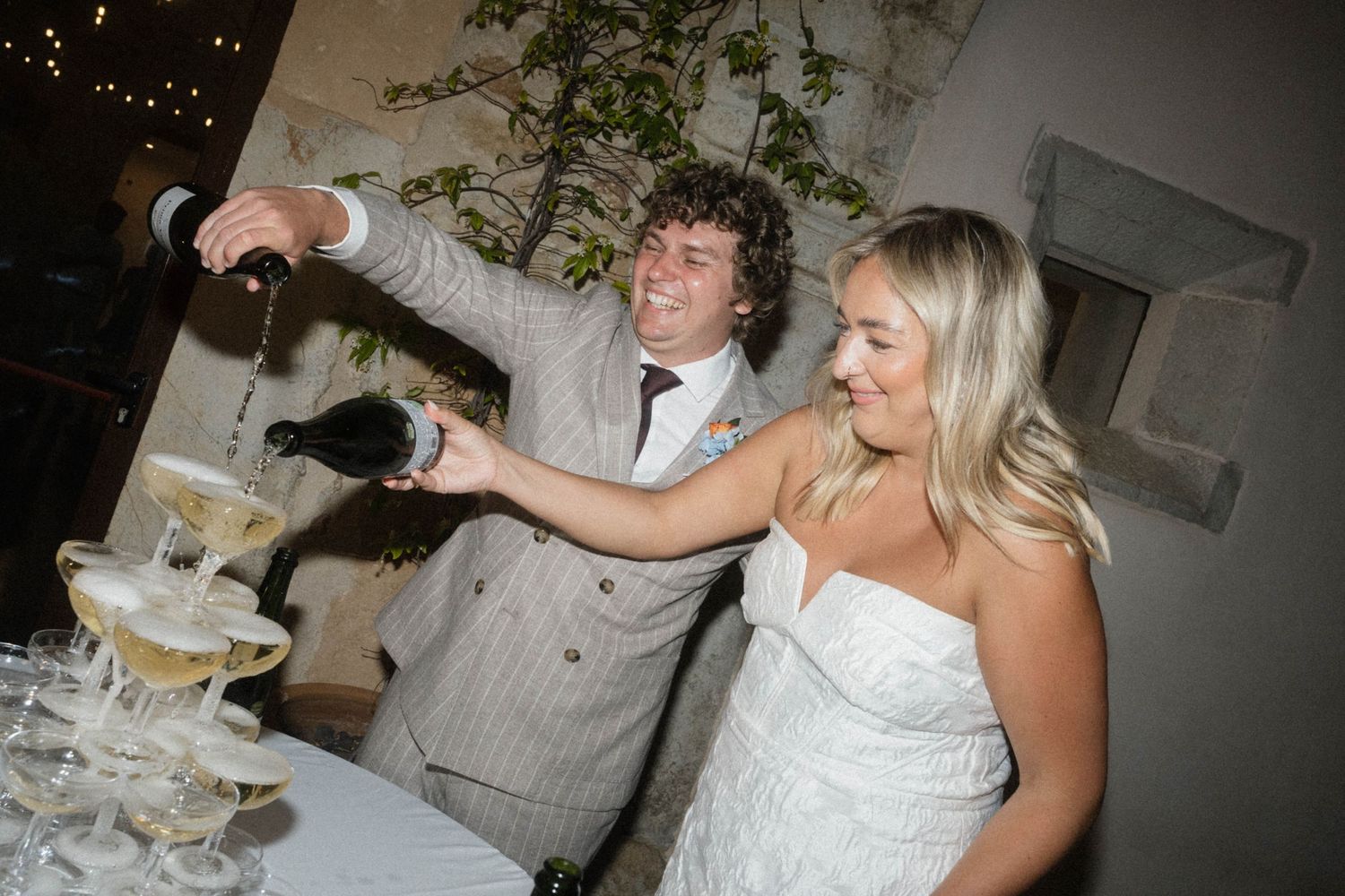 Bride and groom pouring champagne tower at wedding reception celebration.