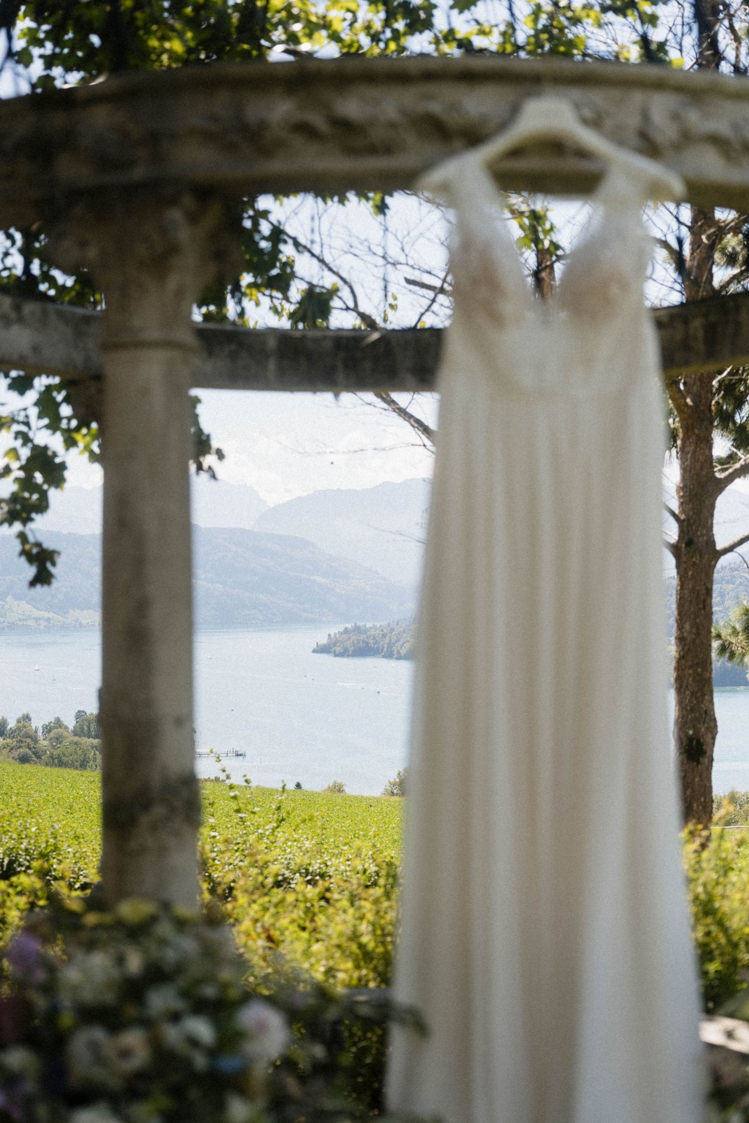 White wedding dress hanging under stone gazebo with lake and mountain views.