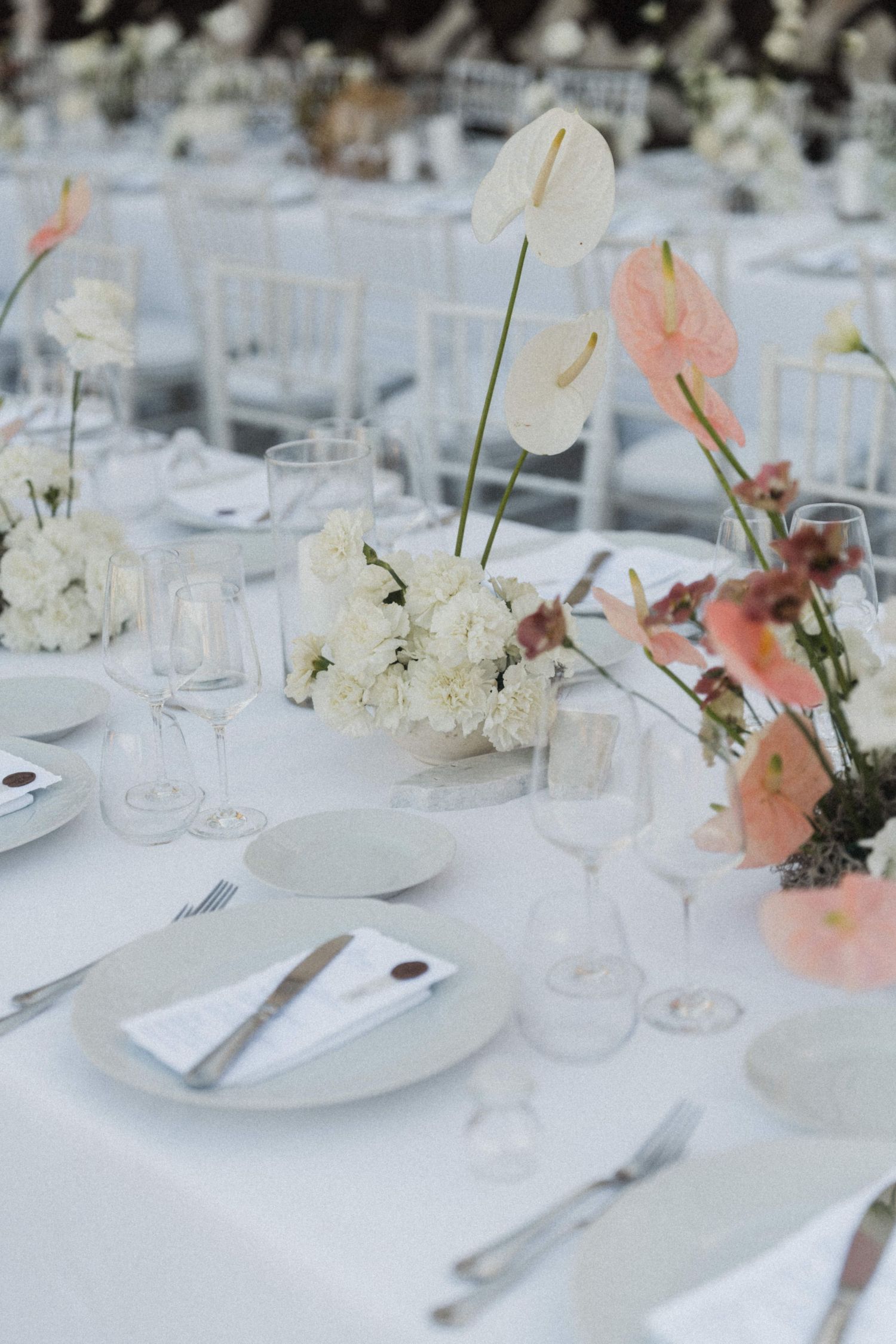 Elegant wedding reception table with white anthurium flowers, crystal glasses and white place settings.