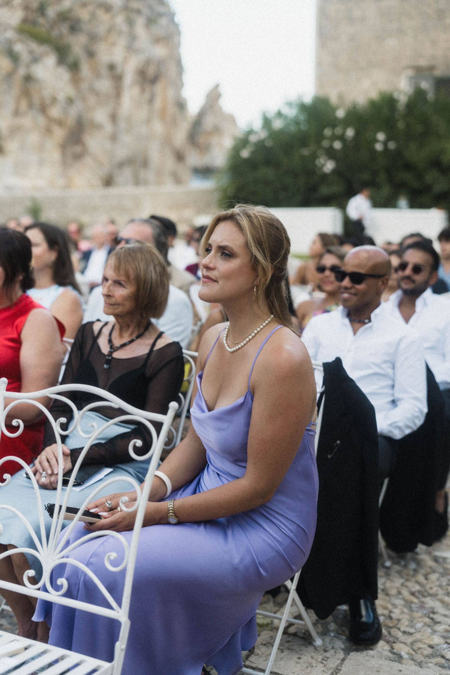 Elegant wedding guest in lavender slip dress seated at outdoor ceremony.