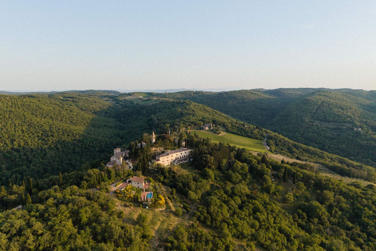 Aerial view of an elegant castle venue nestled among lush green rolling hills under a clear blue sky.