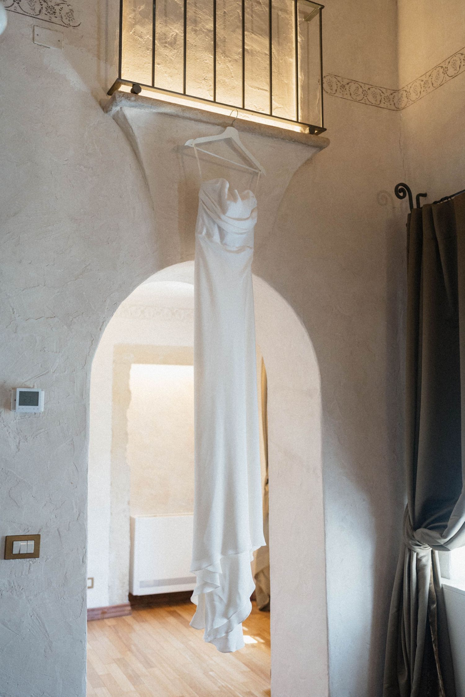 A elegant white wedding dress hanging from a balcony railing over an arched doorway in a rustic venue.