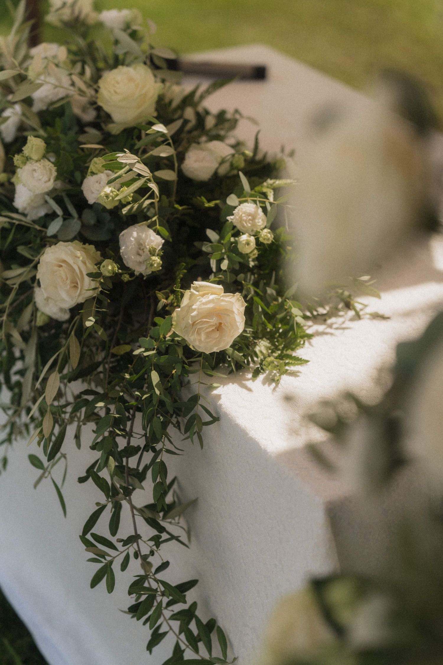 Elegant wedding table arrangement with white roses and lush green foliage cascading over a white linen cloth.