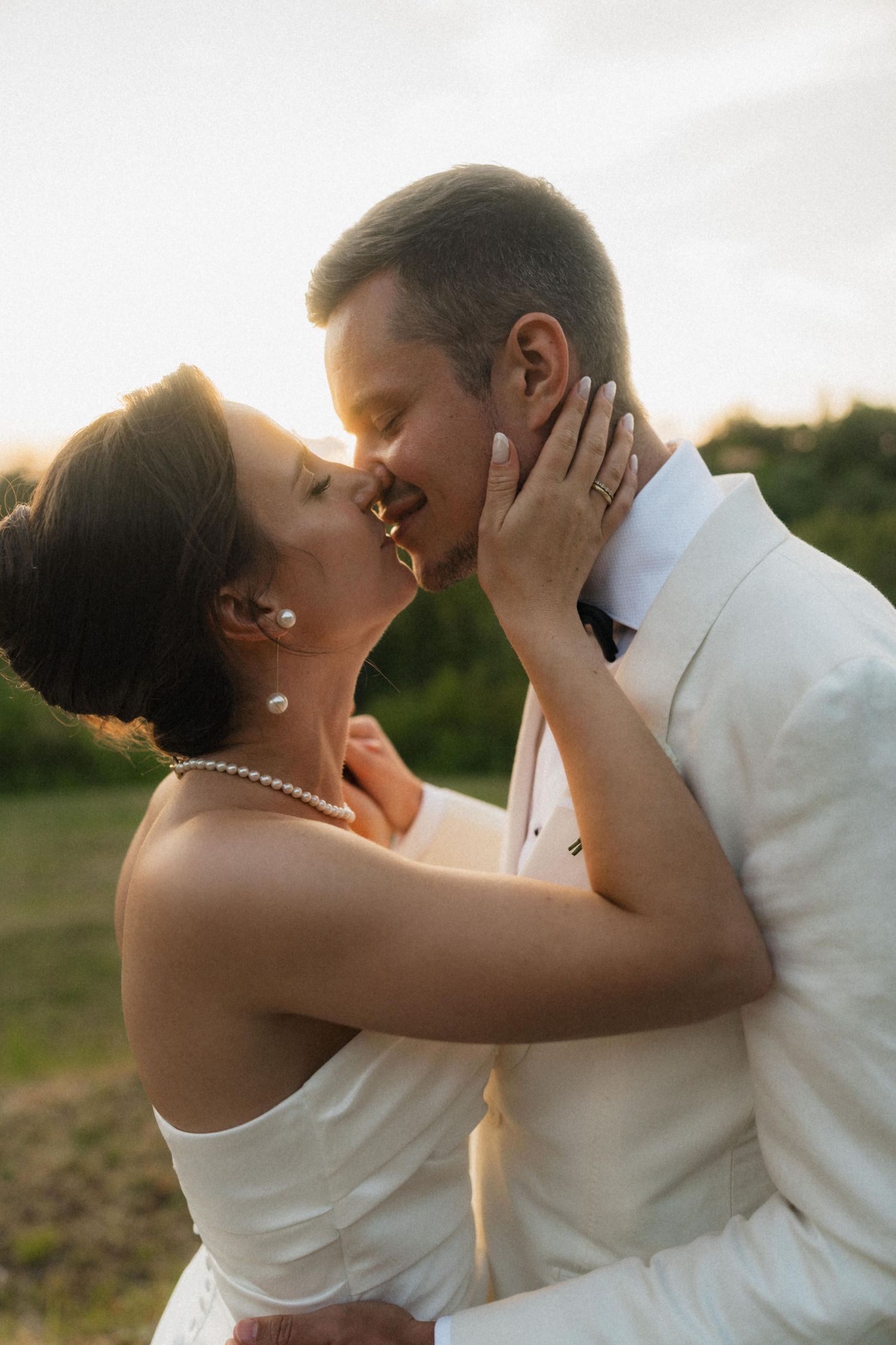 Bride and groom sharing a romantic kiss at golden hour during outdoor wedding.