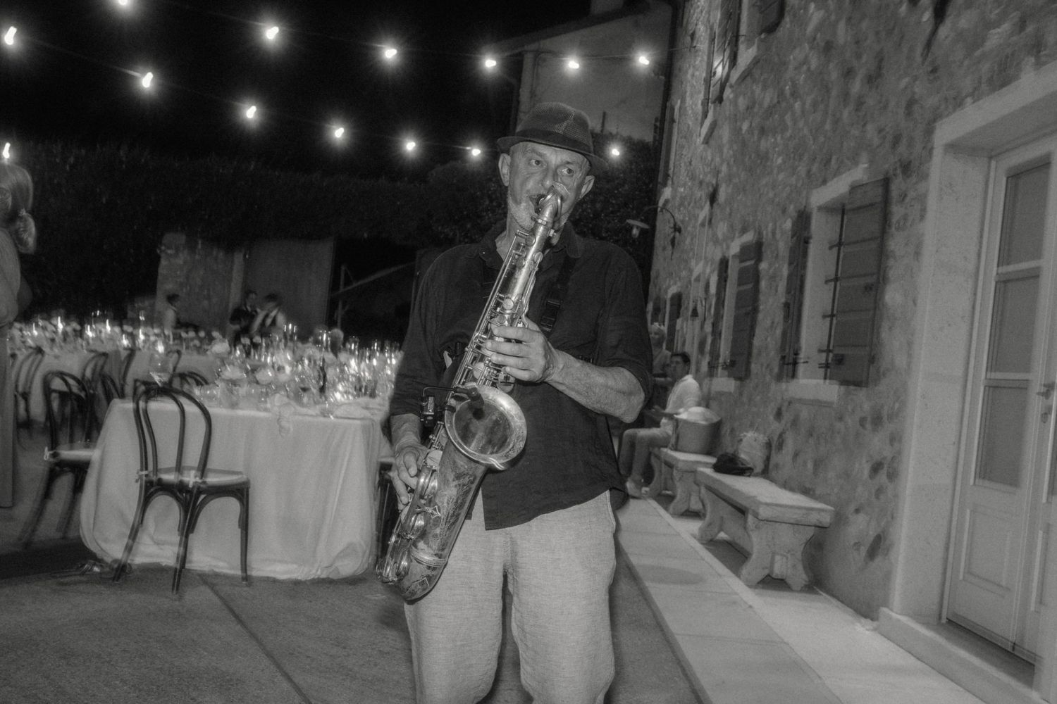 Black and white photo of saxophonist performing at outdoor evening wedding reception.
