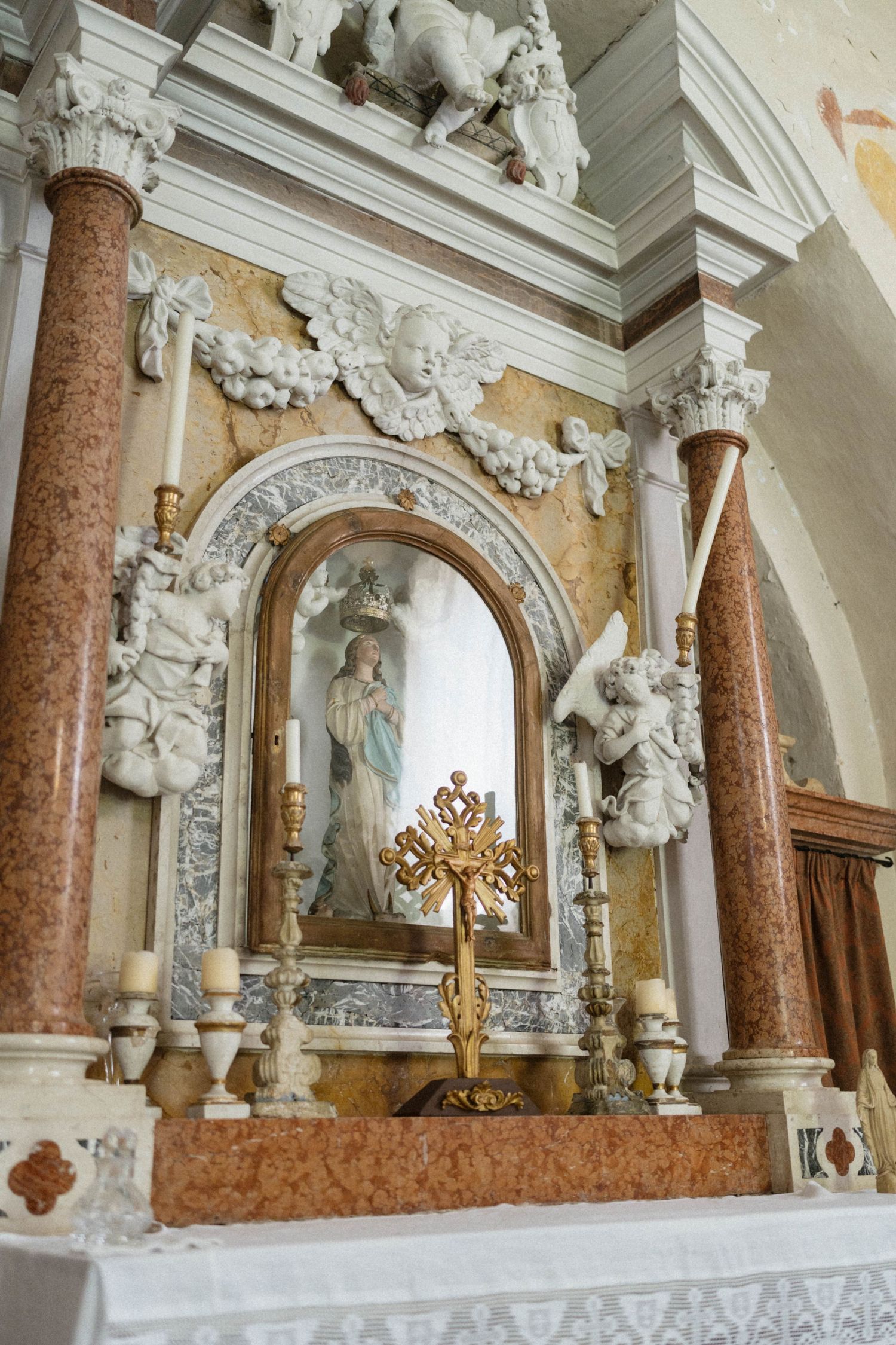 Ornate Catholic church altar with golden cross, marble columns, angel sculptures, and Virgin Mary statue in decorative niche.