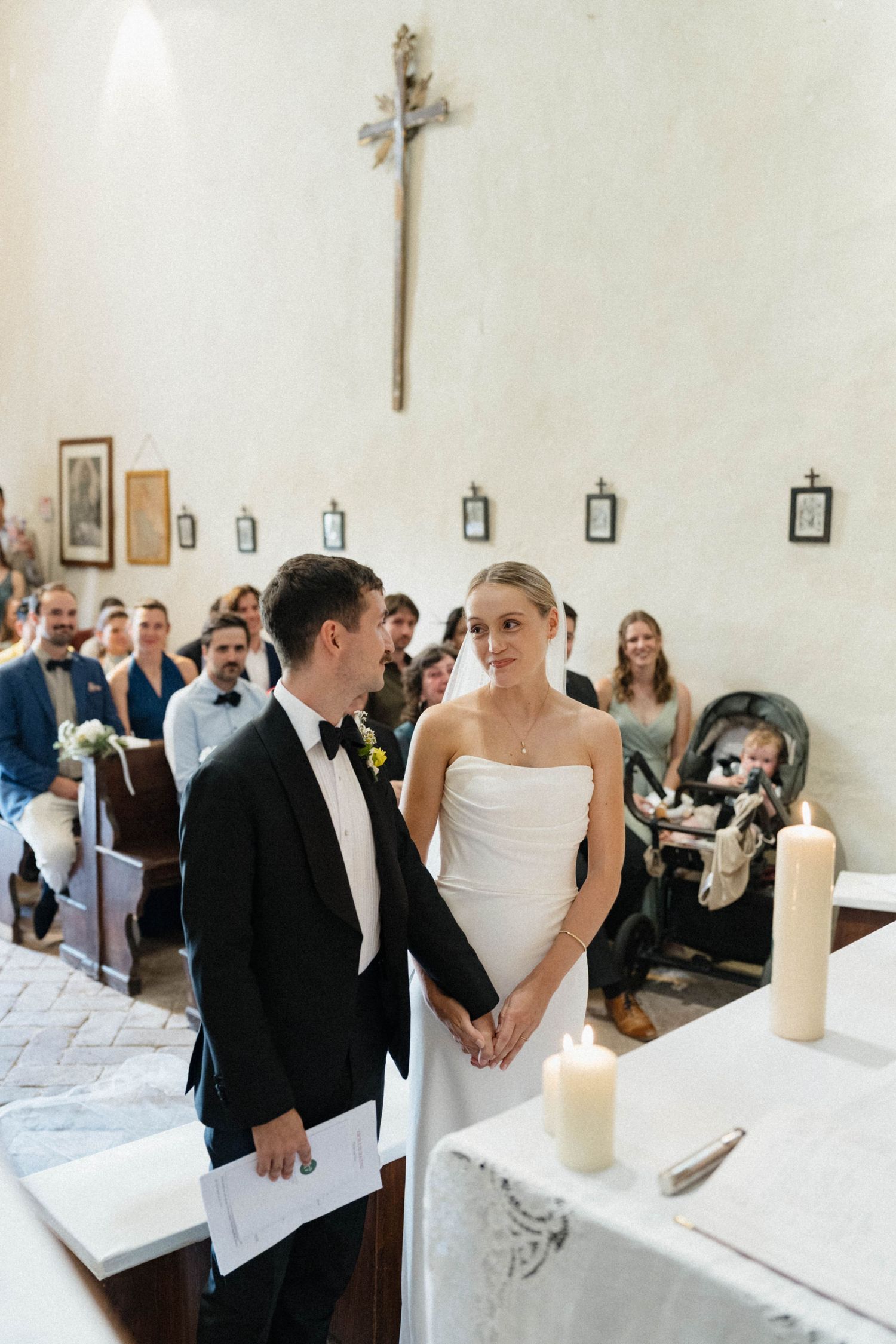 Bride and groom exchange vows at church altar during wedding ceremony with guests seated in pews behind them.