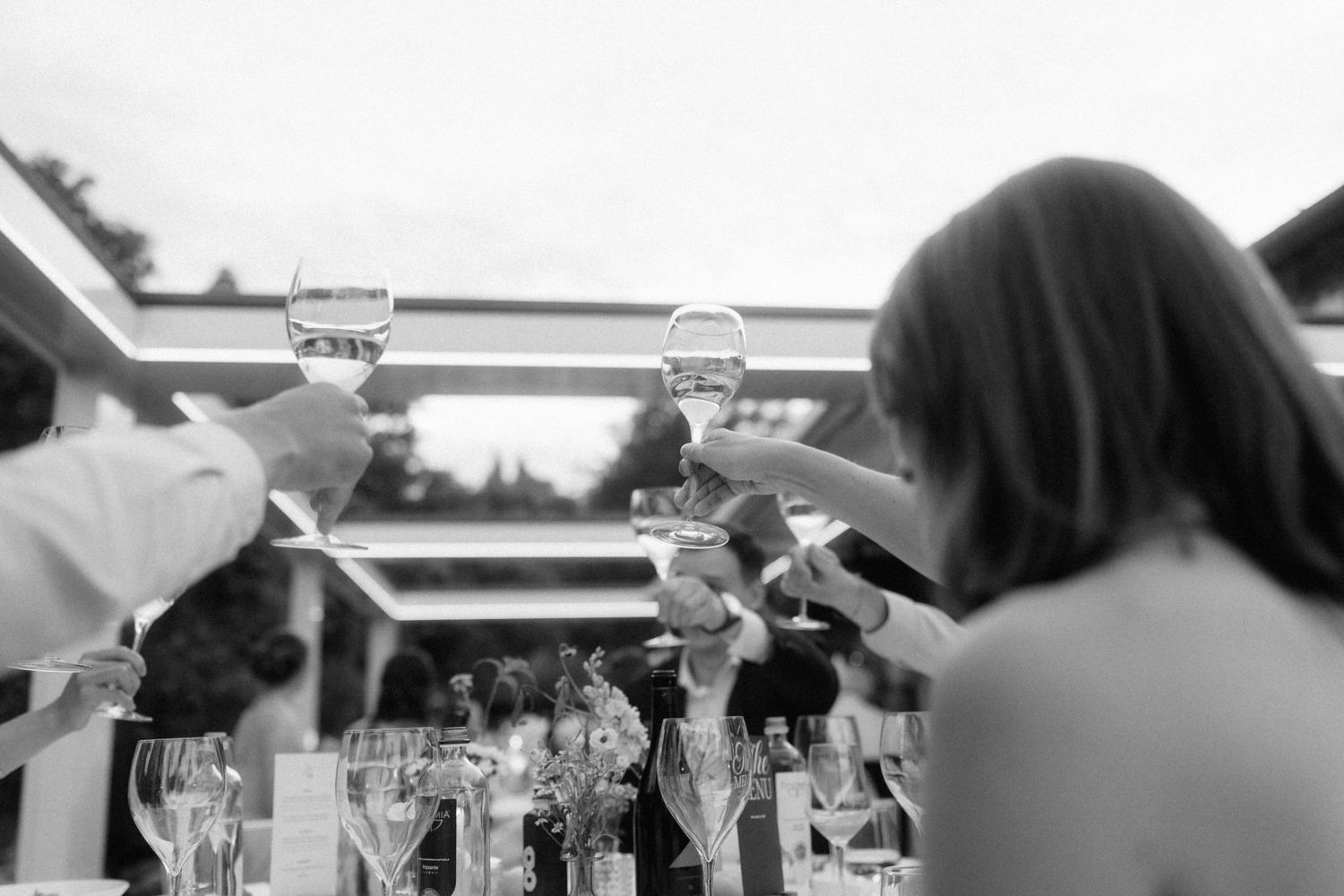Black and white photo of wedding guests raising champagne glasses in a celebratory toast at a reception.