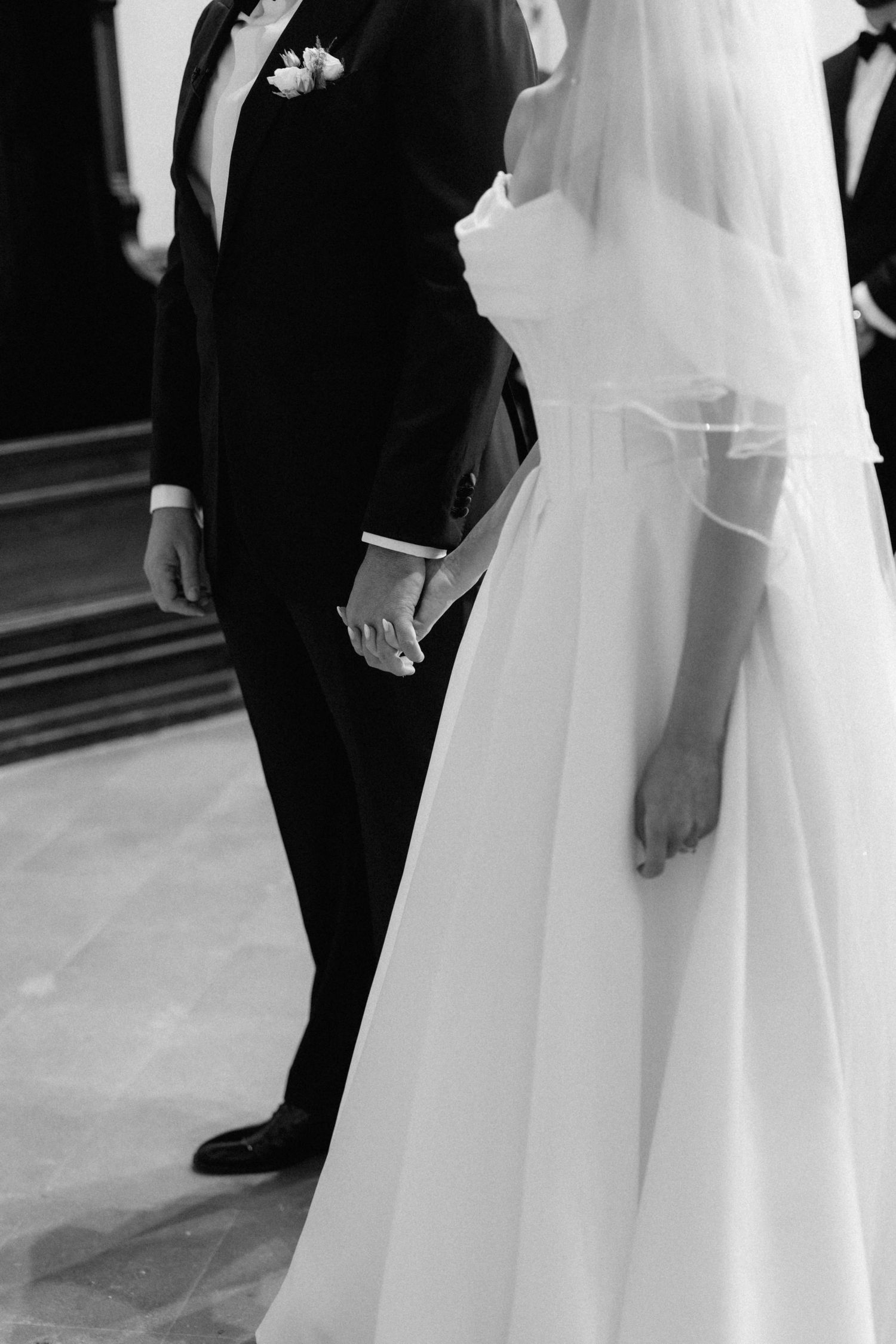 Bride and groom hold hands during wedding ceremony, captured in elegant black and white.