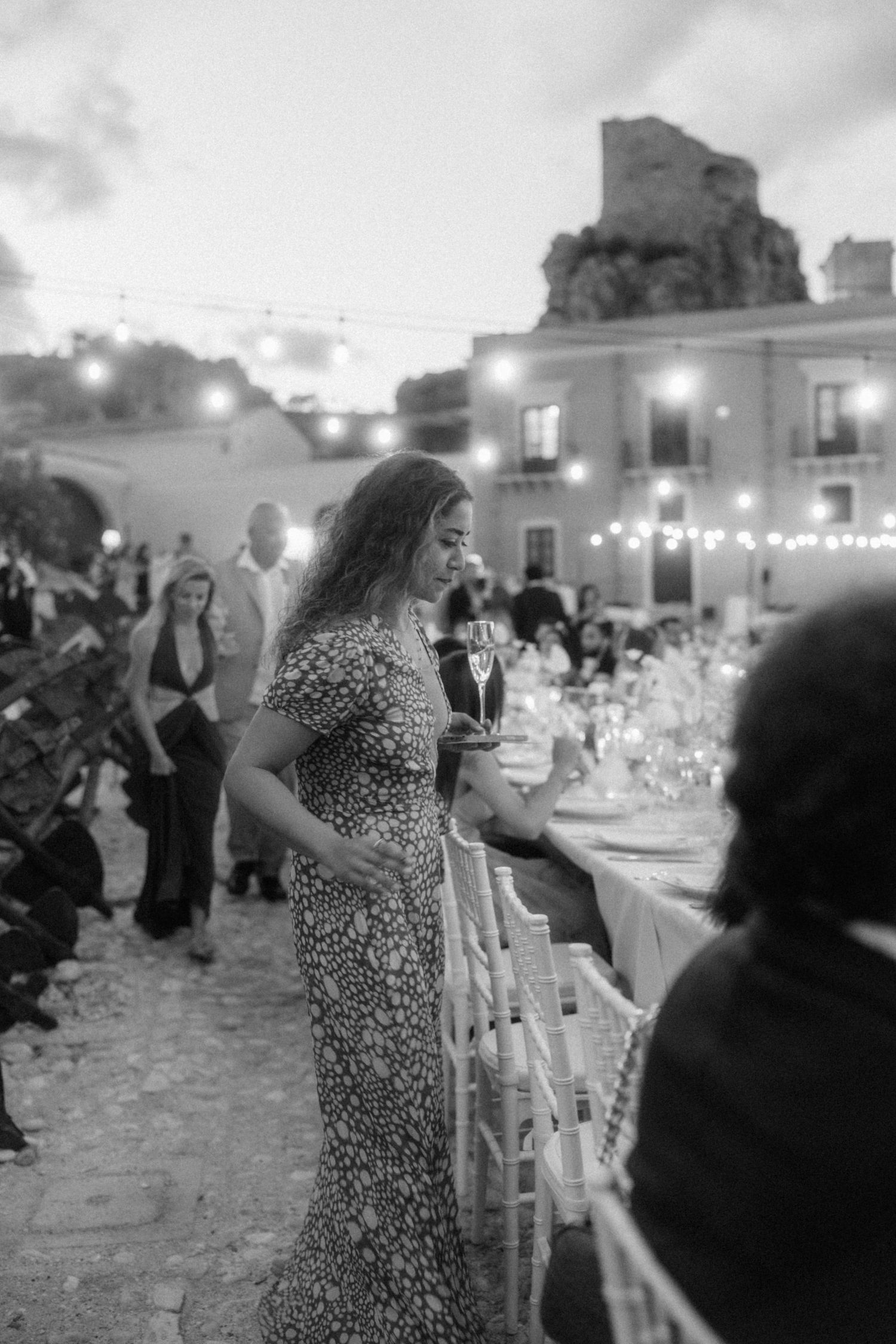 Black and white photo of a woman holding champagne at an outdoor evening wedding reception.