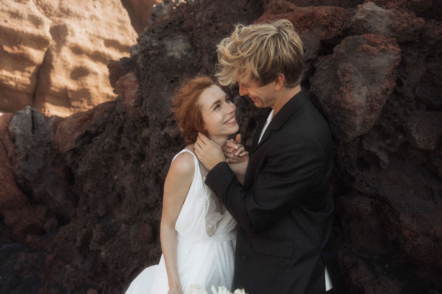 Bride and groom embracing tenderly against red volcanic rocks in an intimate wedding portrait.