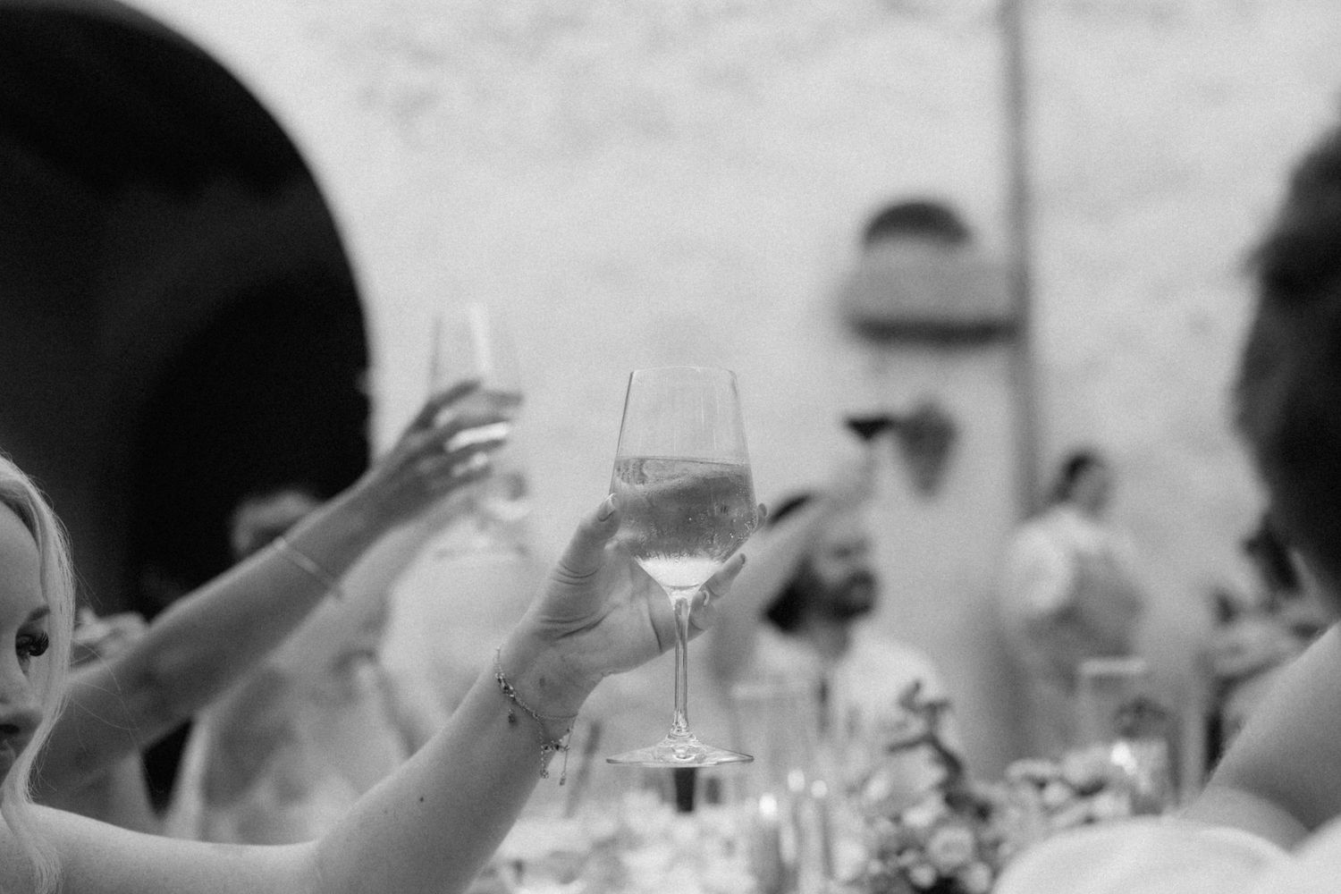 Black and white photo of guests raising champagne glasses in a toast at an elegant wedding reception.