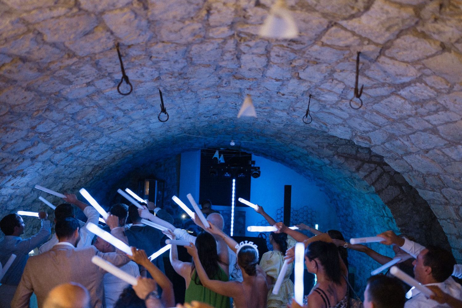 Party guests raising glowing LED sticks under a stone vaulted ceiling at a nightclub event.