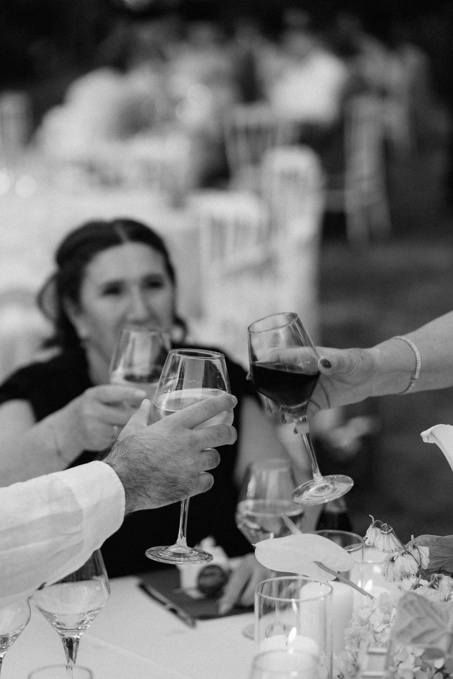 Black and white photo of guests clinking wine glasses at an outdoor wedding reception dinner party.
