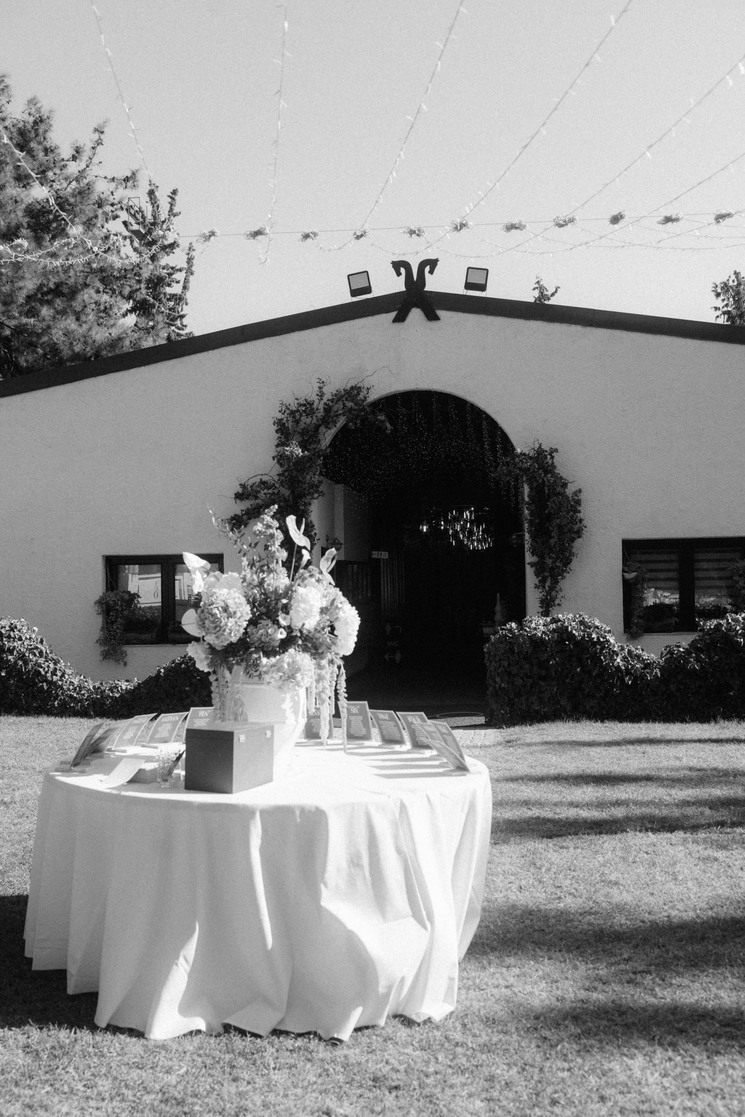Black and white photo of an elegant outdoor wedding reception table with floral arrangement in front of a white Spanish-style venue.