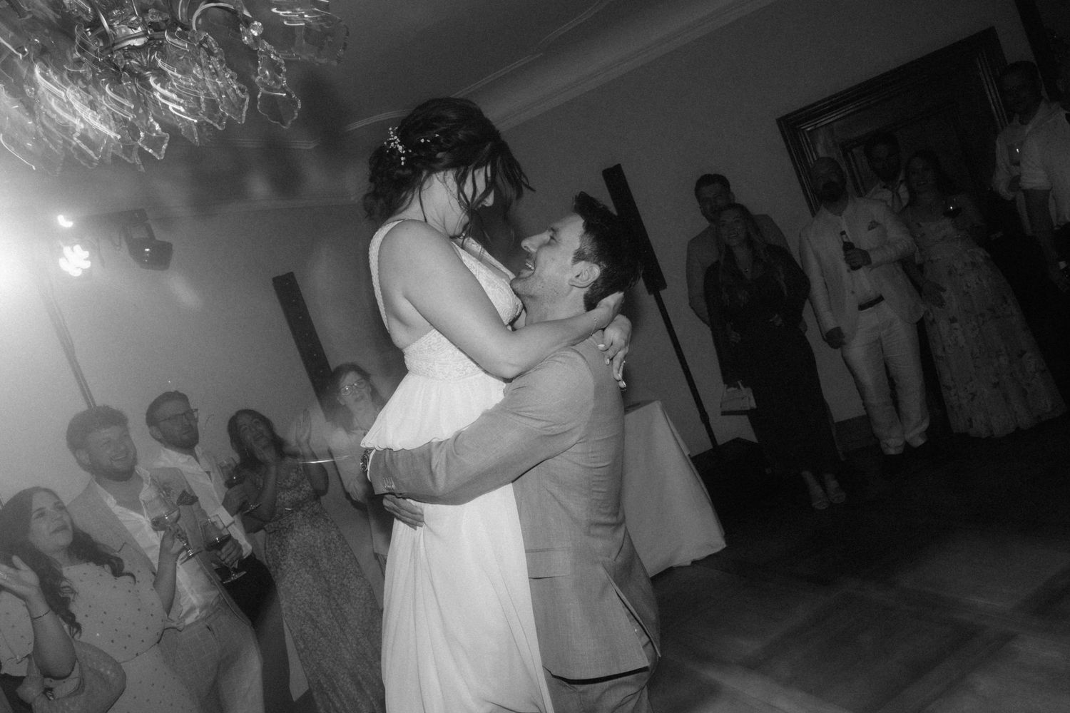 Black and white photo of bride and groom sharing first dance while guests watch at wedding reception.