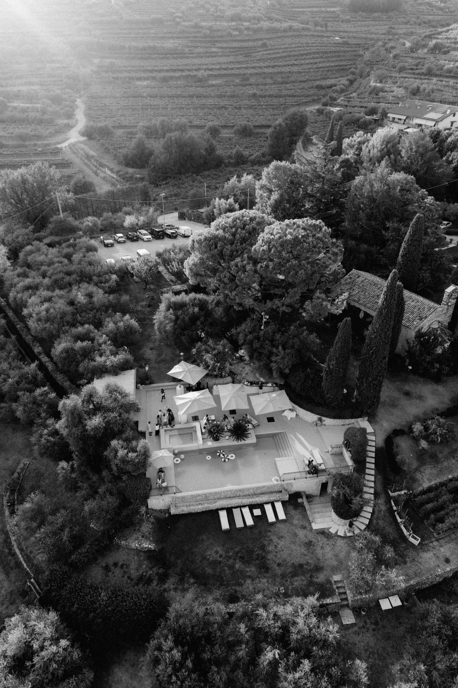 Aerial black and white view of a Tuscan villa surrounded by vineyards and cypress trees with wedding guests.