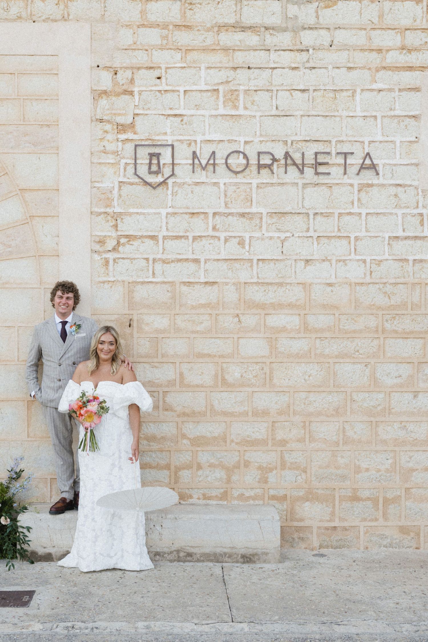 Bride and groom posing in front of a limestone wall with Morneta wedding venue sign.