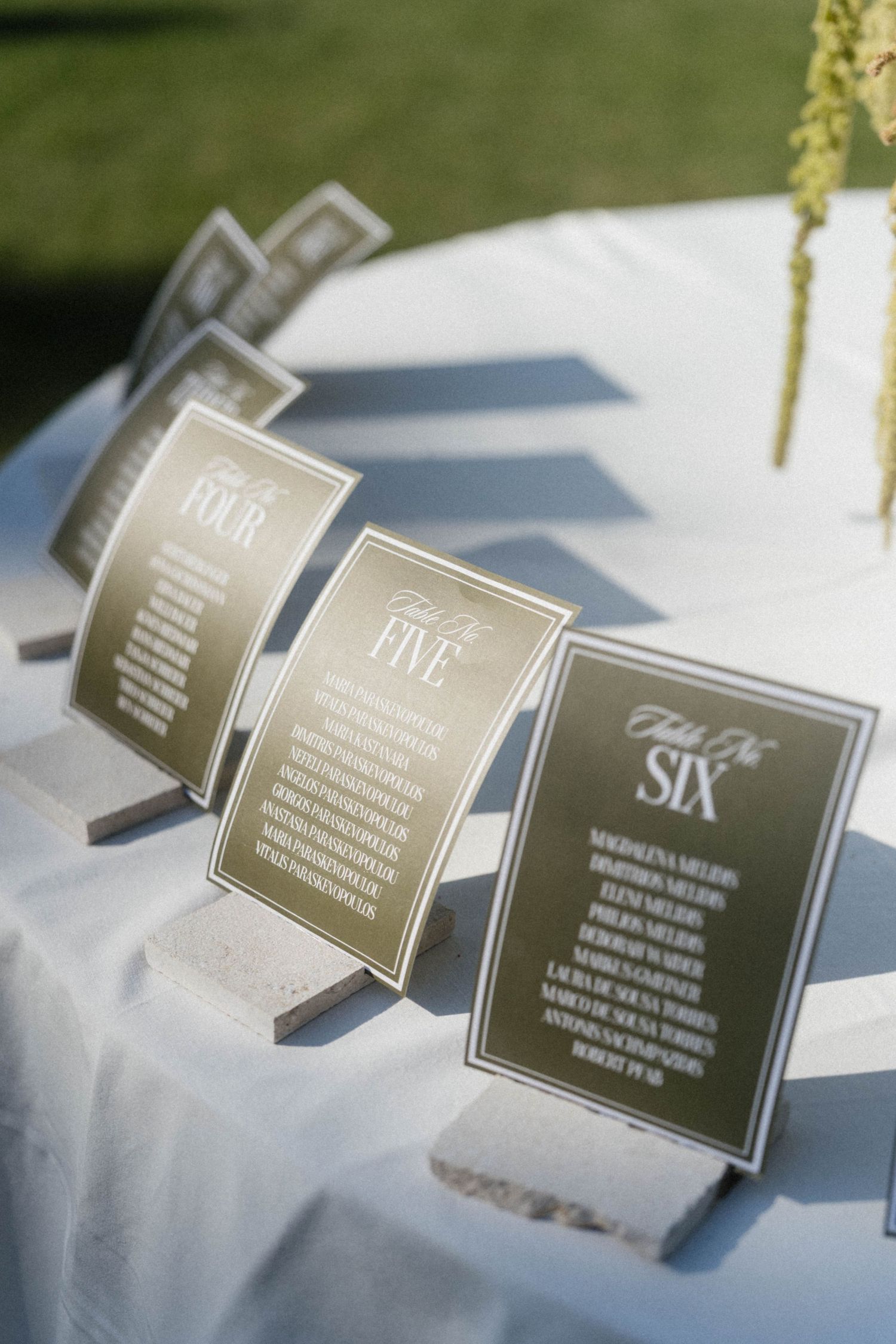 Close-up of olive green and white wedding table seating chart cards numbered four through six on stone stands.