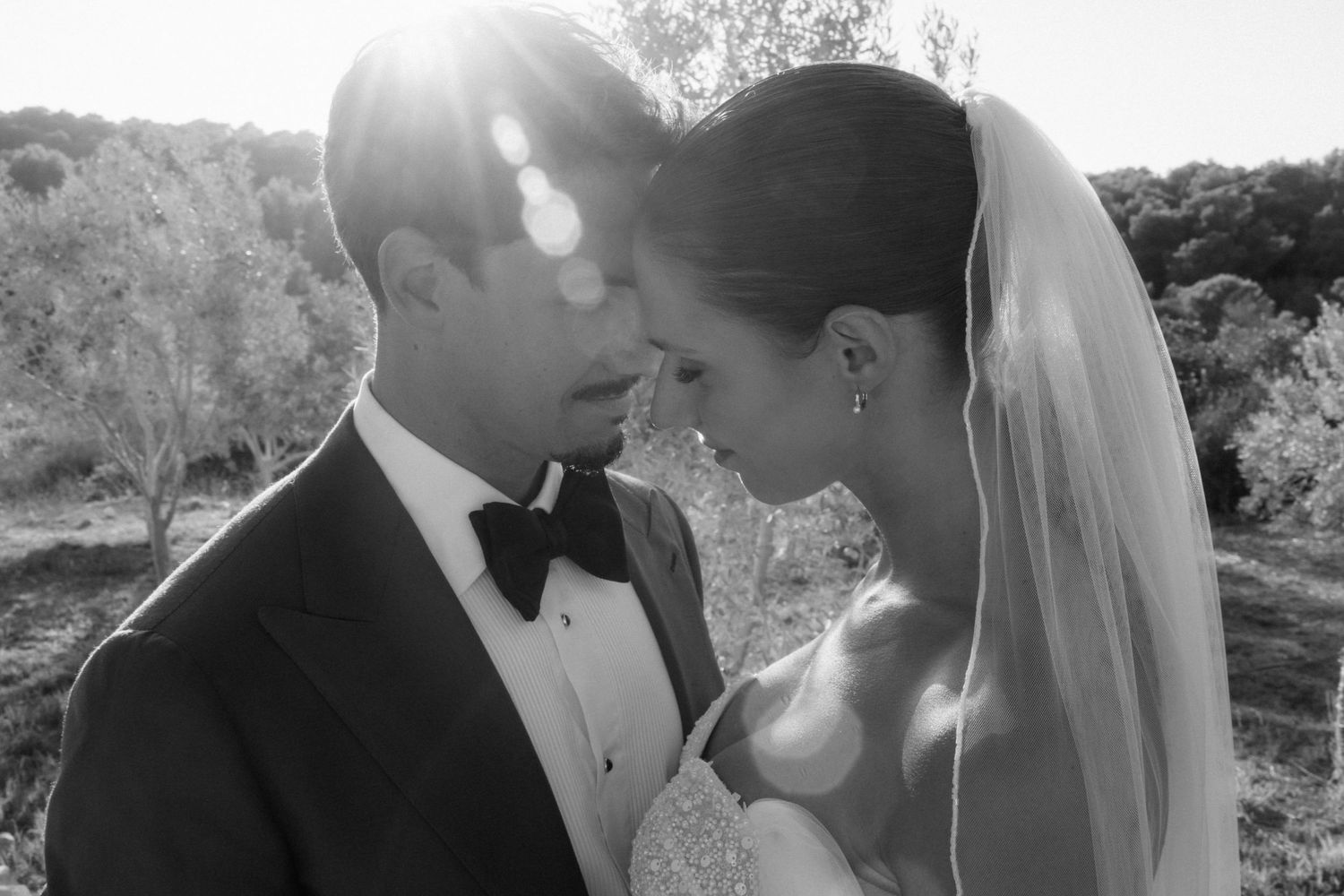 Black and white close-up of the groom in a bow tie and the bride in a veil touching foreheads in a tender moment.