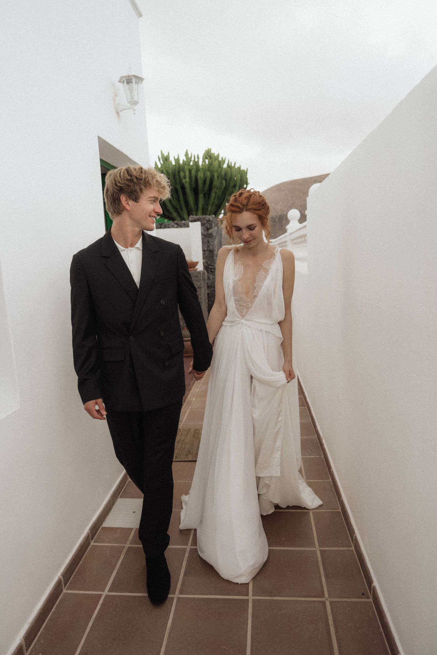 Bride and groom walking hand in hand through white corridor in elegant wedding attire.