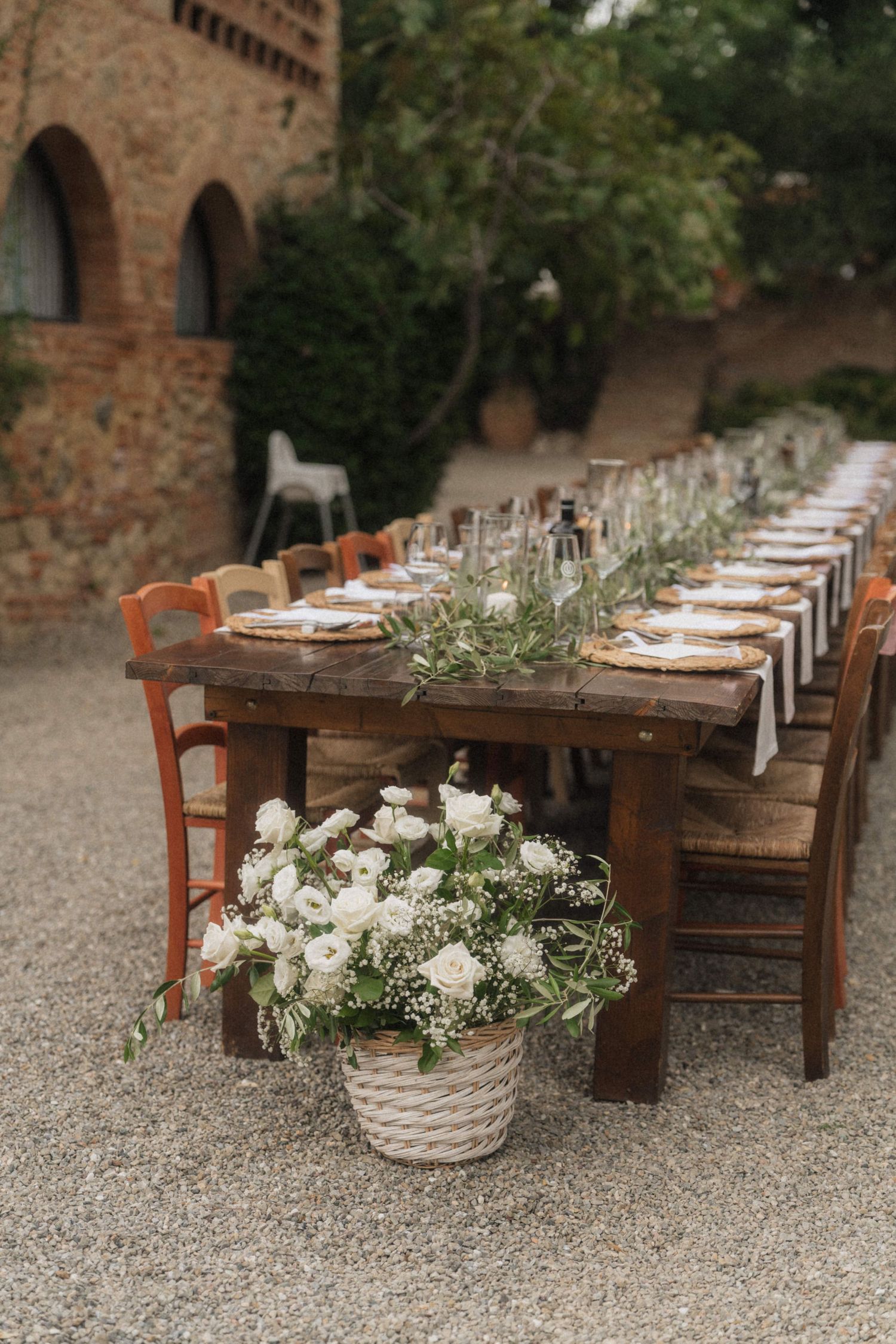 Long rustic wooden outdoor wedding reception table with white floral basket centerpiece at Tuscan venue.
