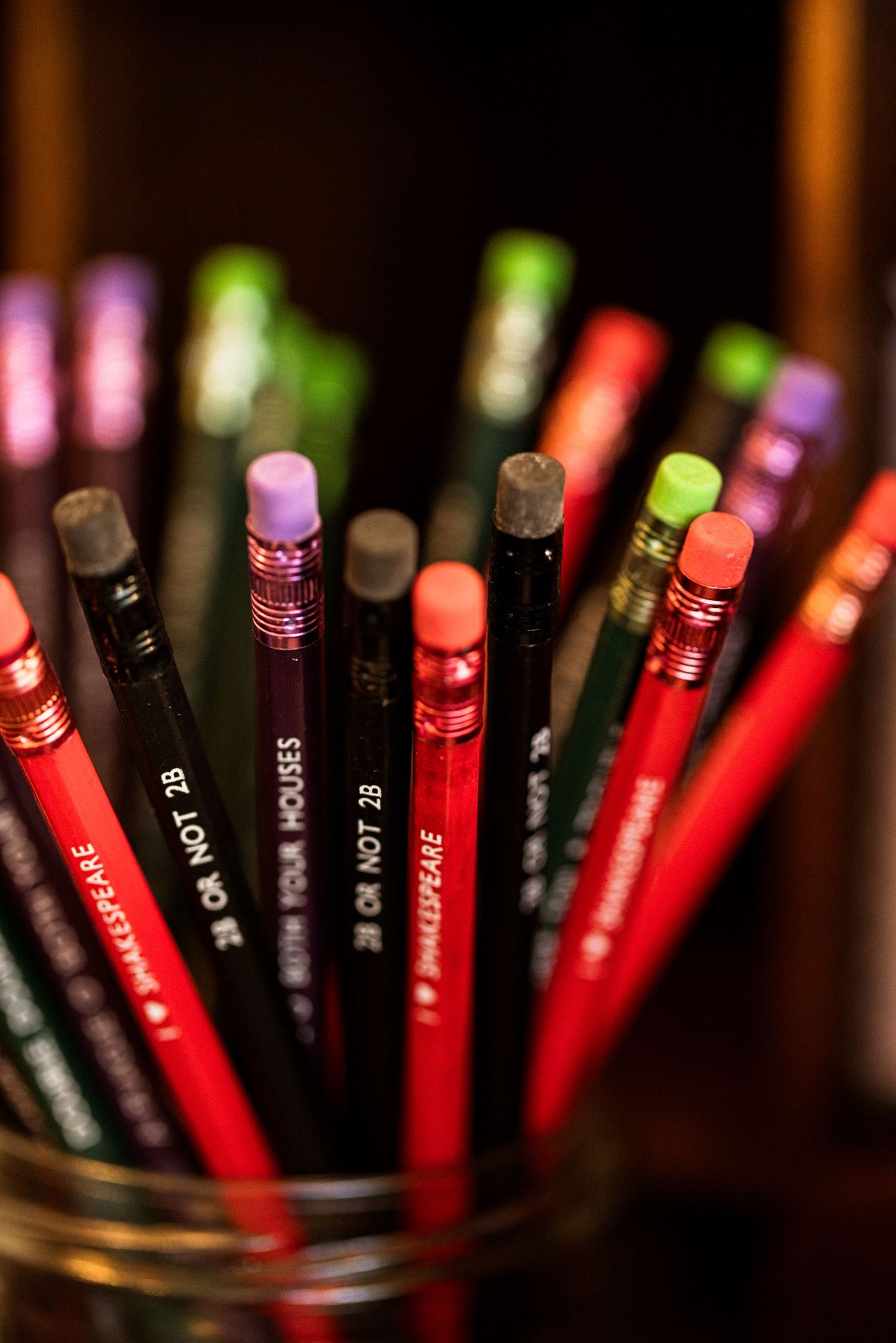 Collection of red and black Shakespeare-themed pencils with colorful erasers in a jar.