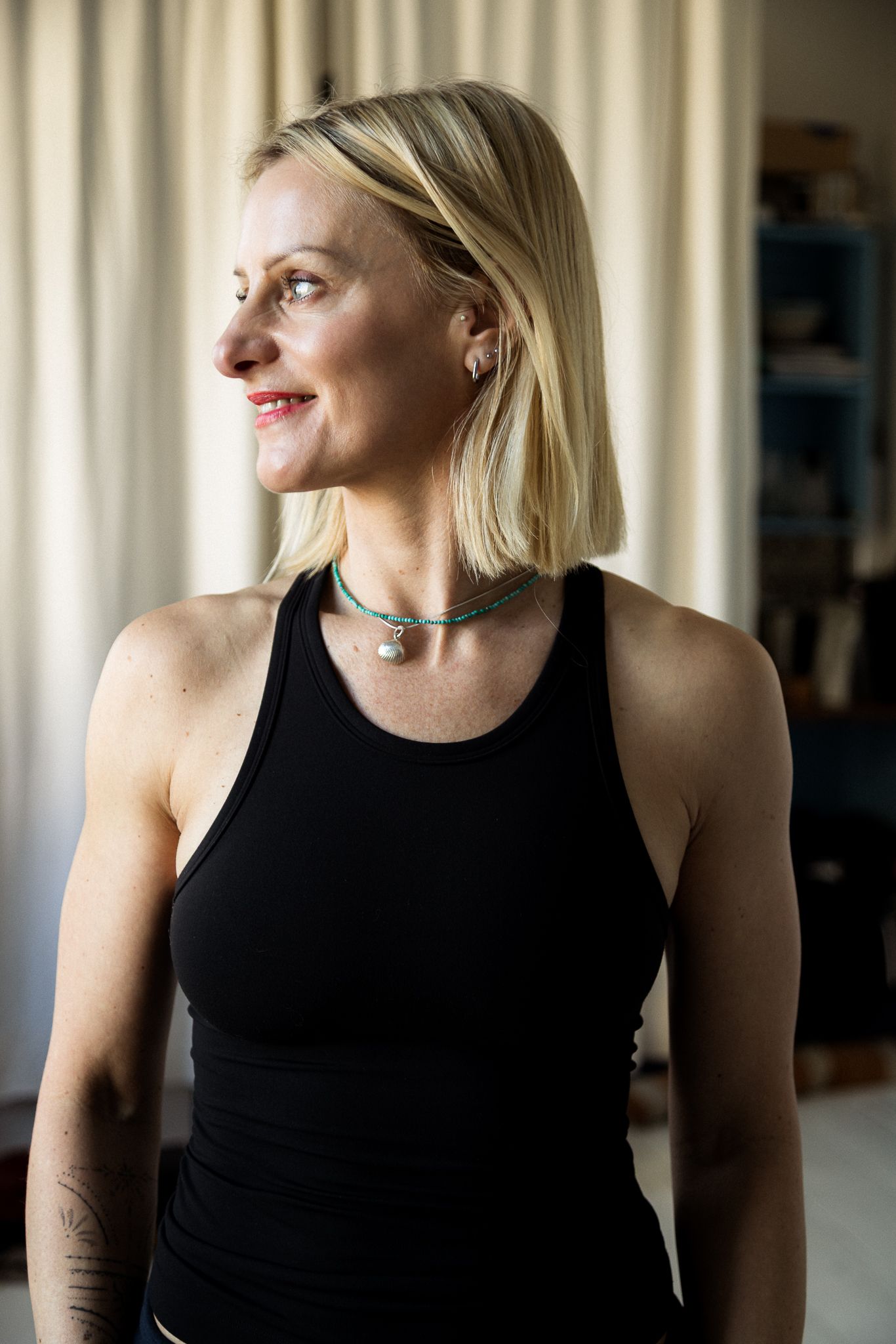 Blonde woman in black tank top with choker necklace smiling indoors.