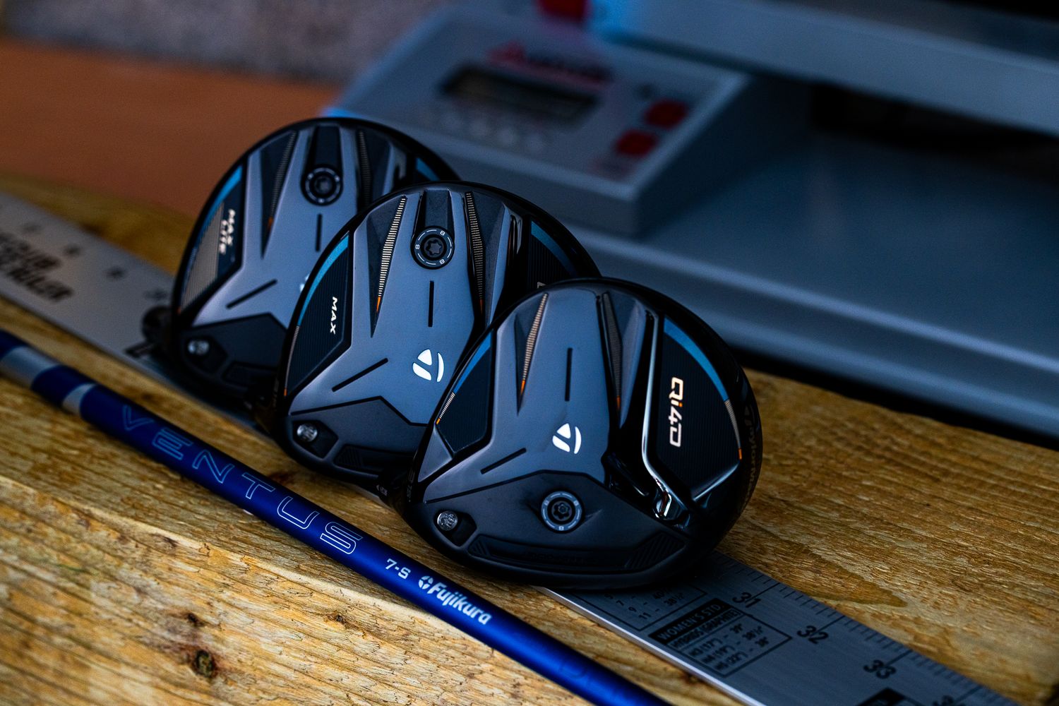 Three TaylorMade golf club heads displayed on a wooden surface with a blue shaft.