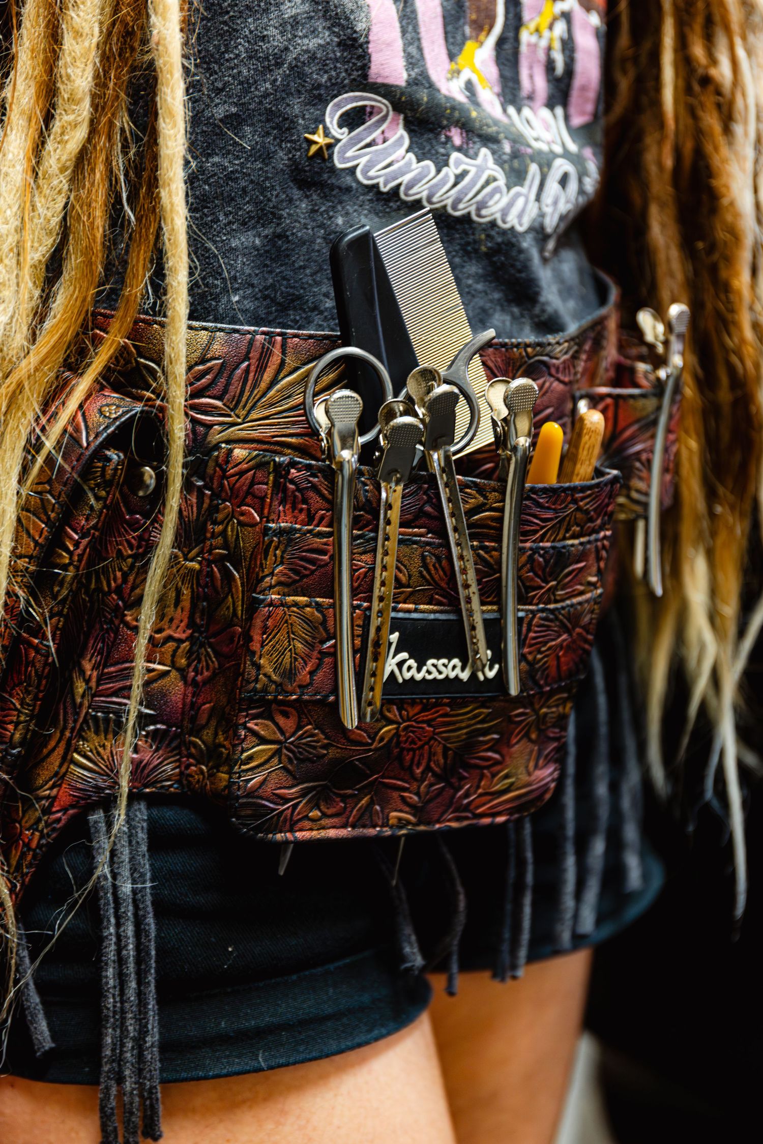 Hairstylist wearing decorative leather tool belt with Kassaku scissors, combs, and styling tools at a hair show.