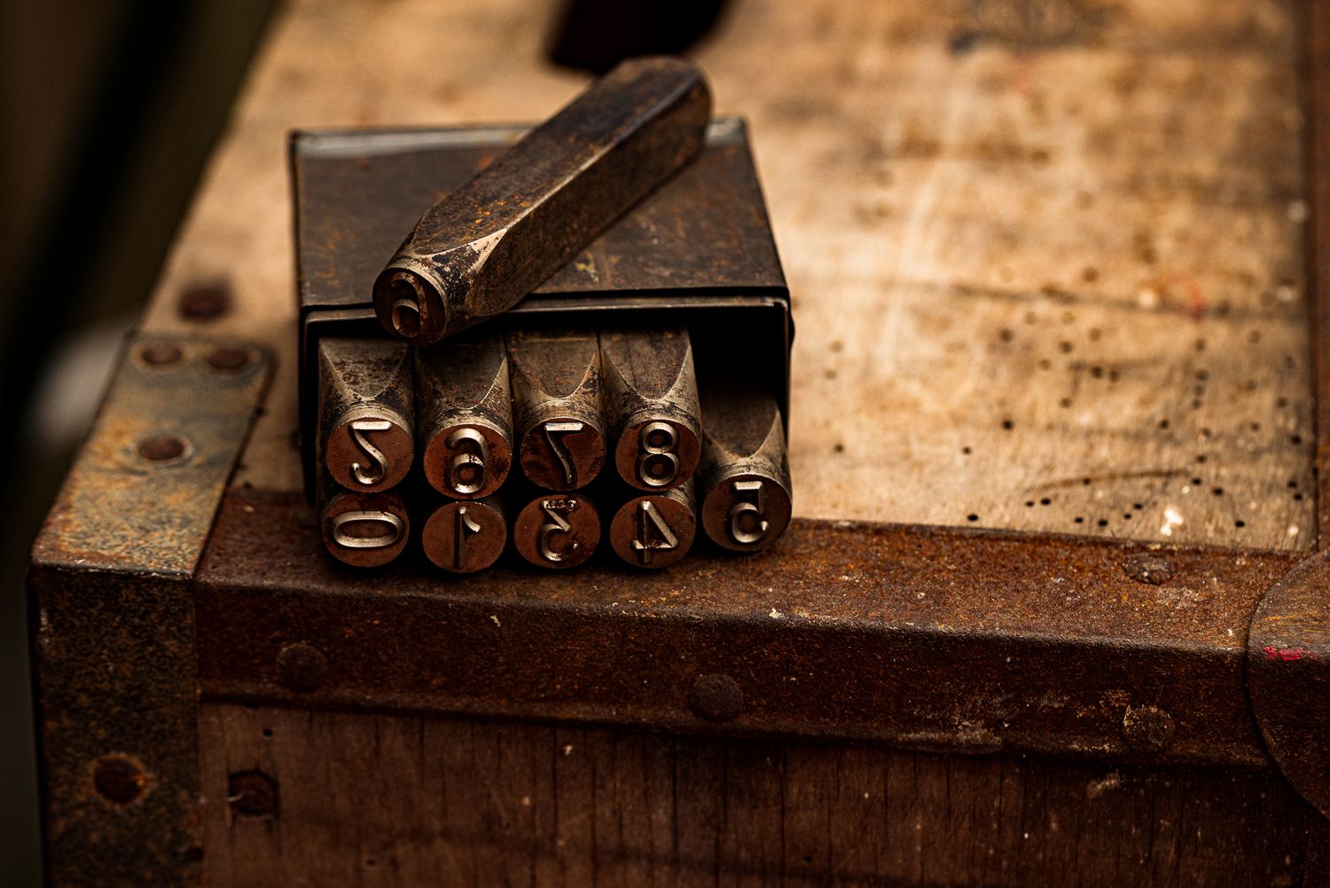 Vintage metal letter stamp set on a worn wooden workbench in a rustic workshop setting.
