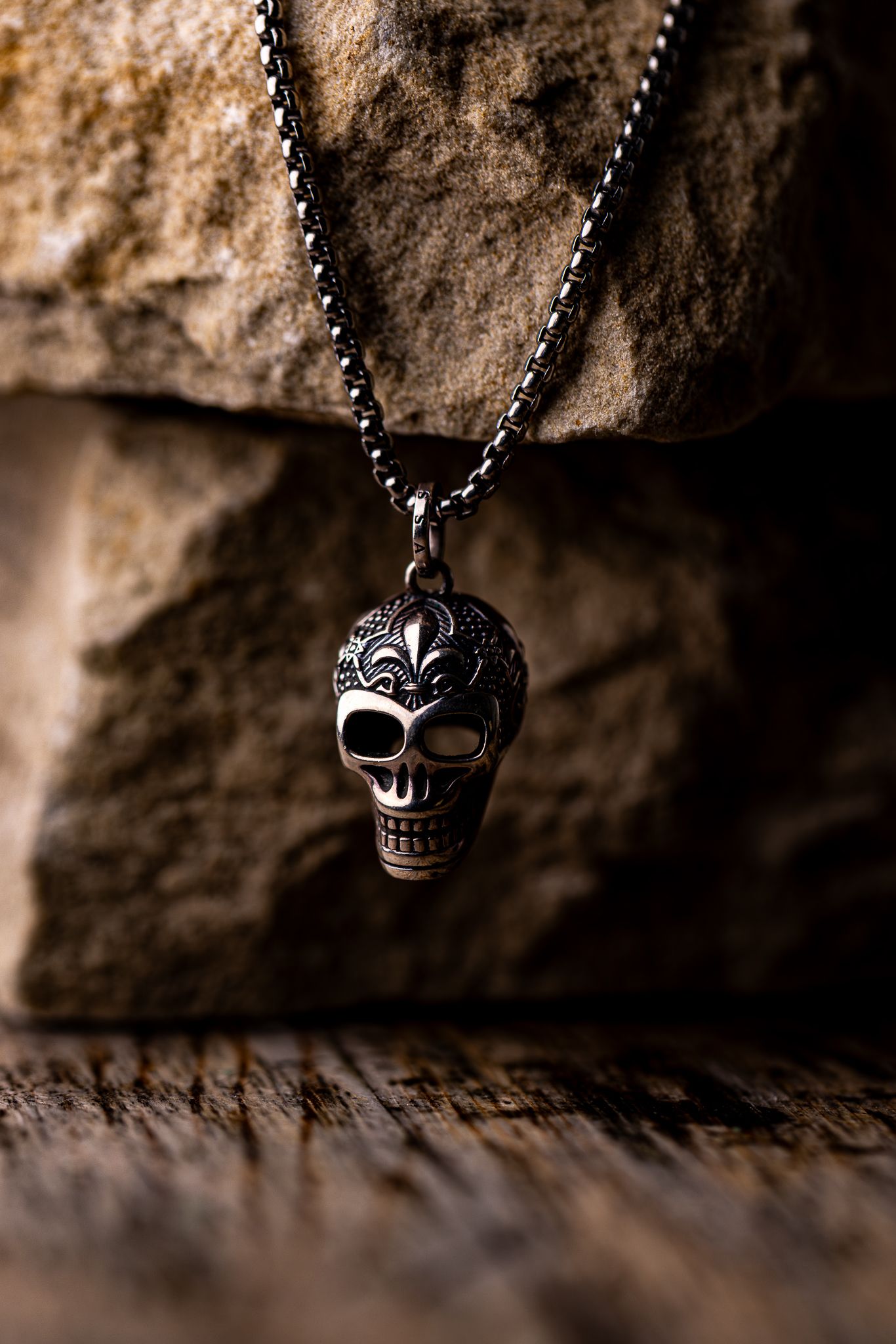 Ornate silver skull pendant necklace displayed against rustic stone and wood background.