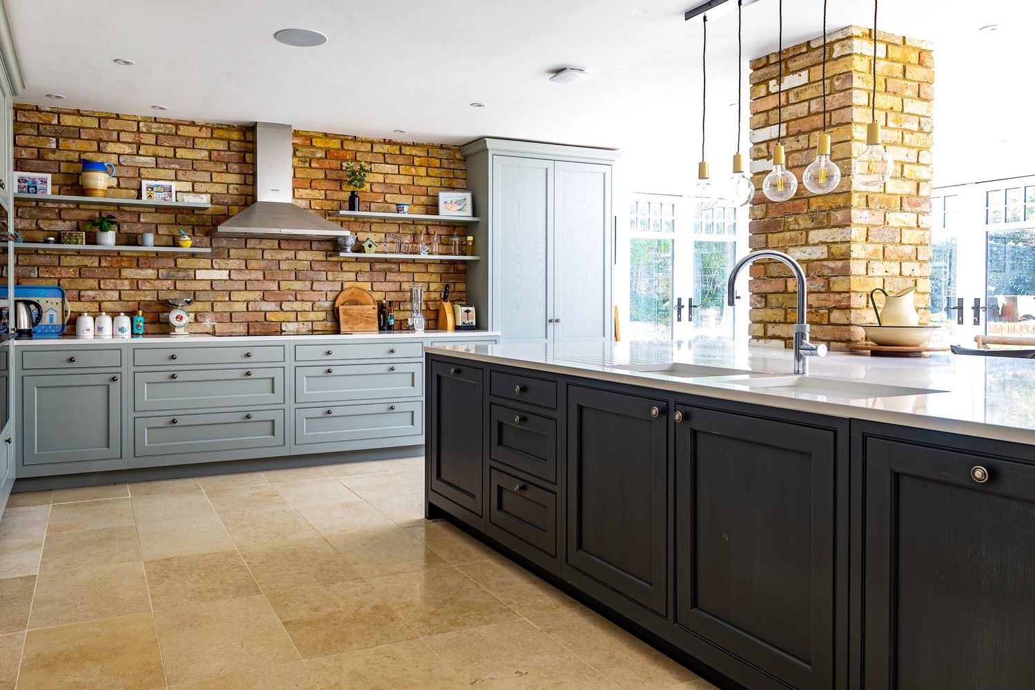 Modern kitchen featuring dark island, sage green cabinets, exposed brick wall, and pendant lighting.