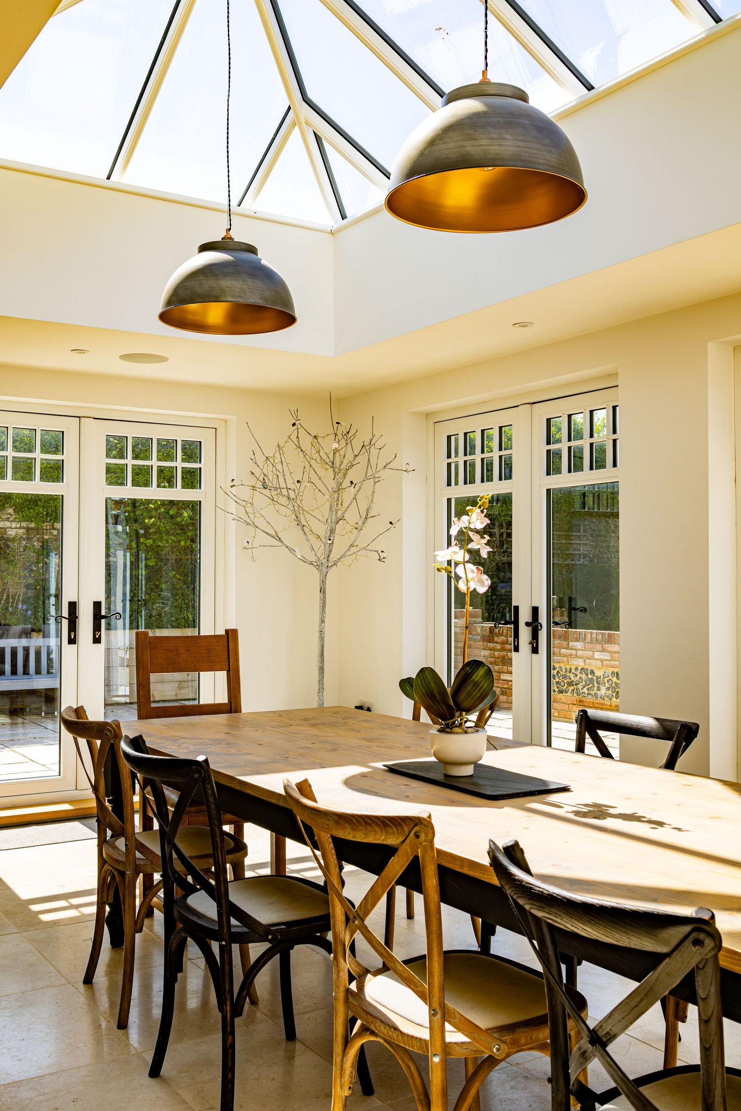 Bright orangery dining room with skylight roof lantern, oval wooden table and industrial pendant lights.