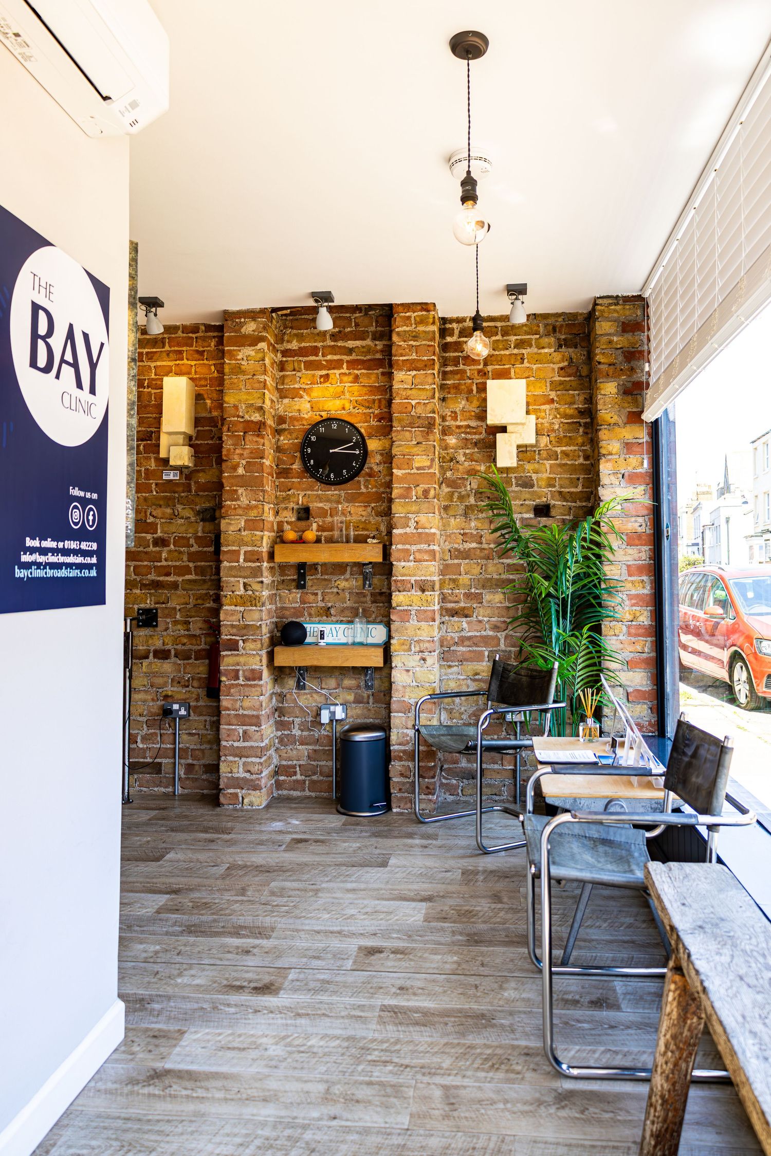 Industrial-style clinic reception area with exposed brick wall, pendant lights, and Bay Clinic signage.