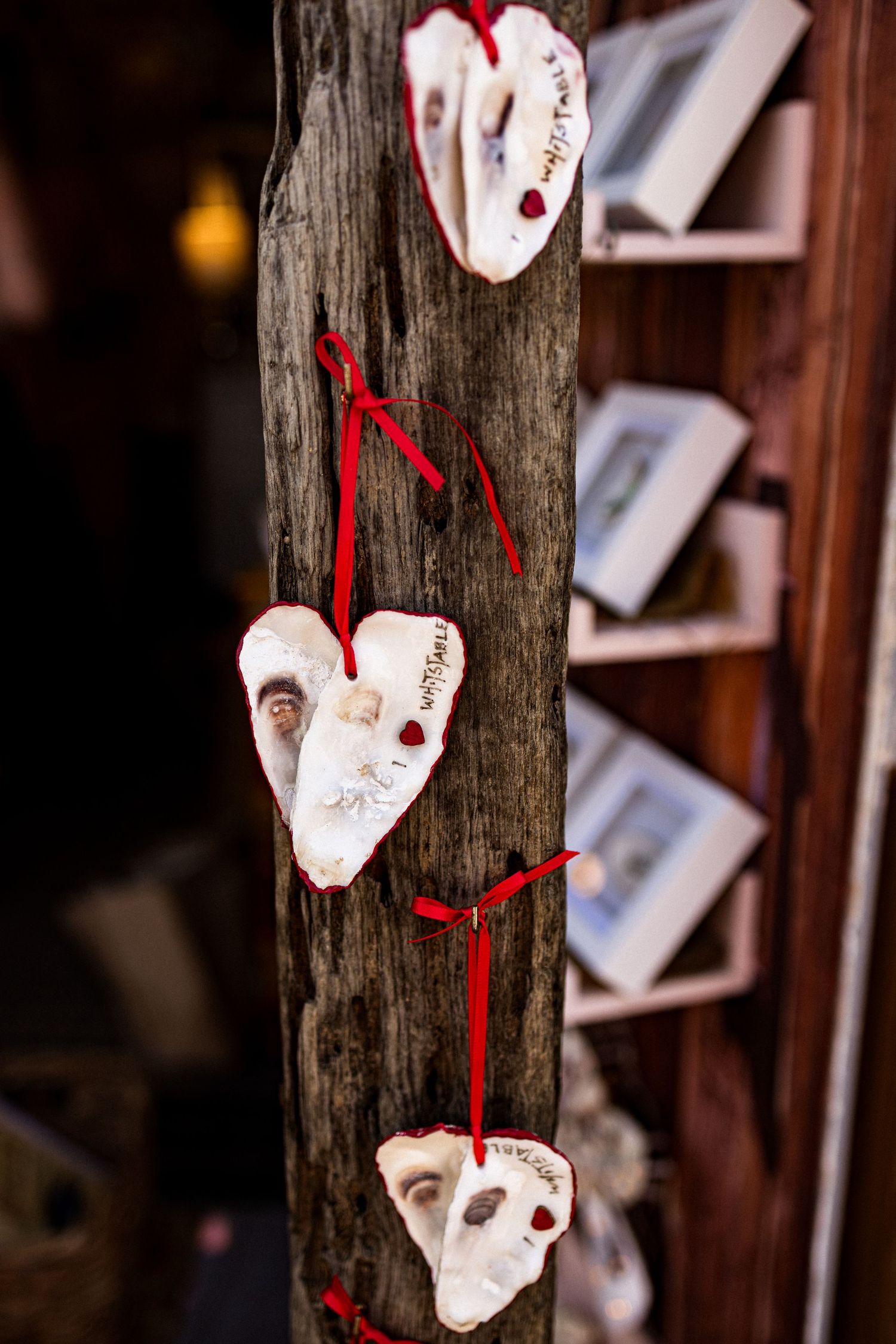 Handmade ceramic heart ornaments with red ribbons hanging on a rustic wooden post in a charming holiday display.