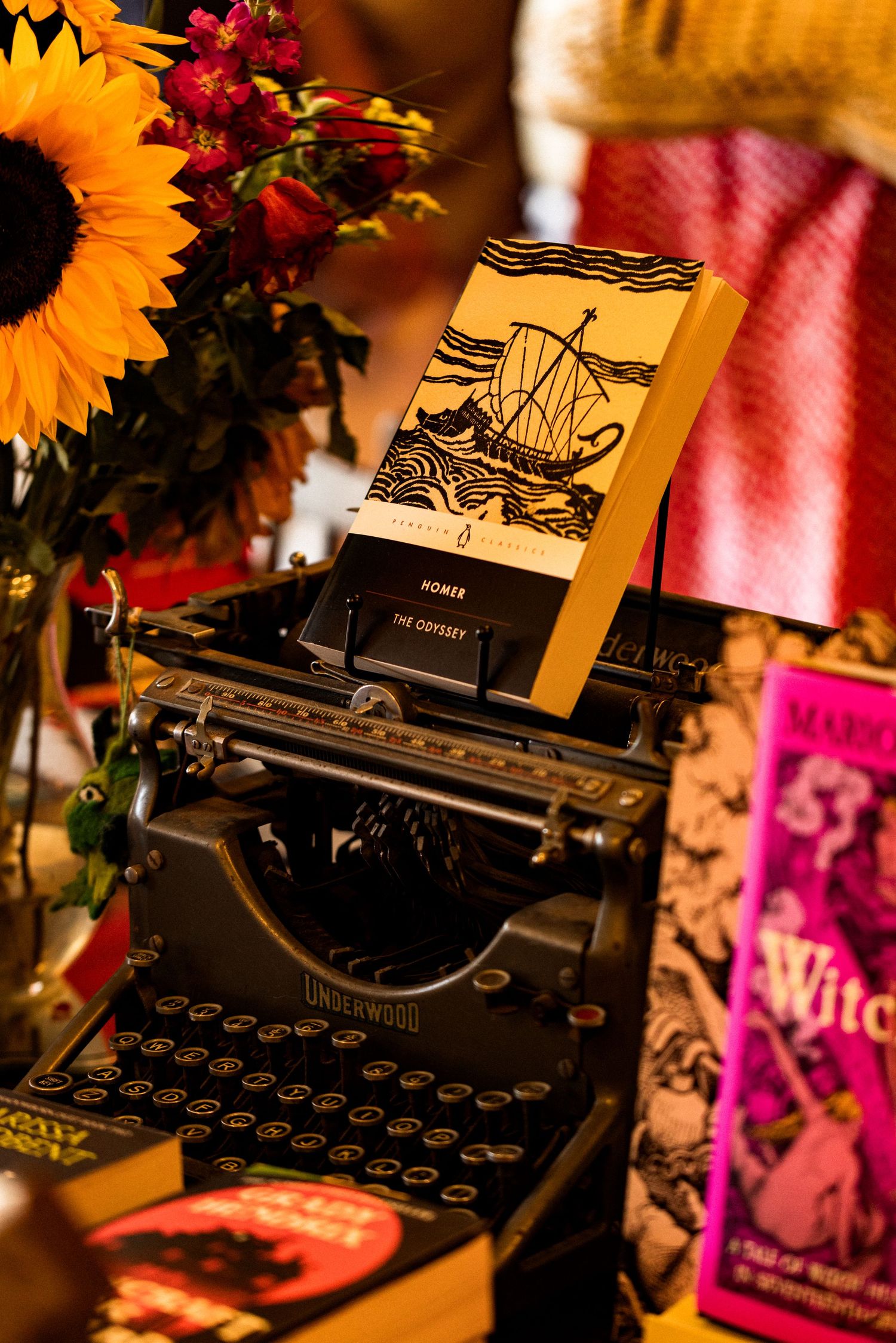 Vintage Underwood typewriter displaying Homer's Odyssey book surrounded by sunflowers and books.