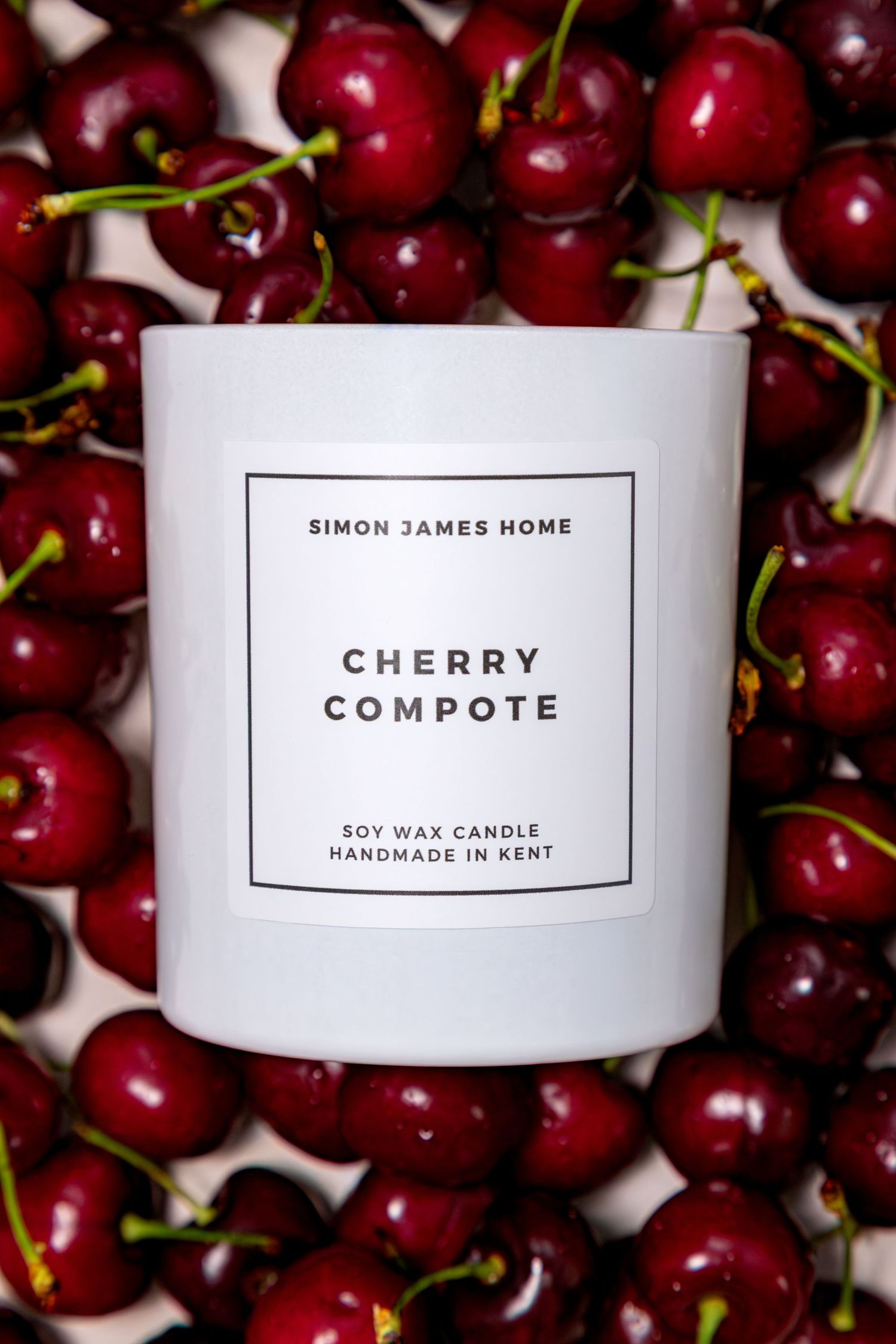 Simon James Home Cherry Compote soy wax candle surrounded by fresh red cherries.