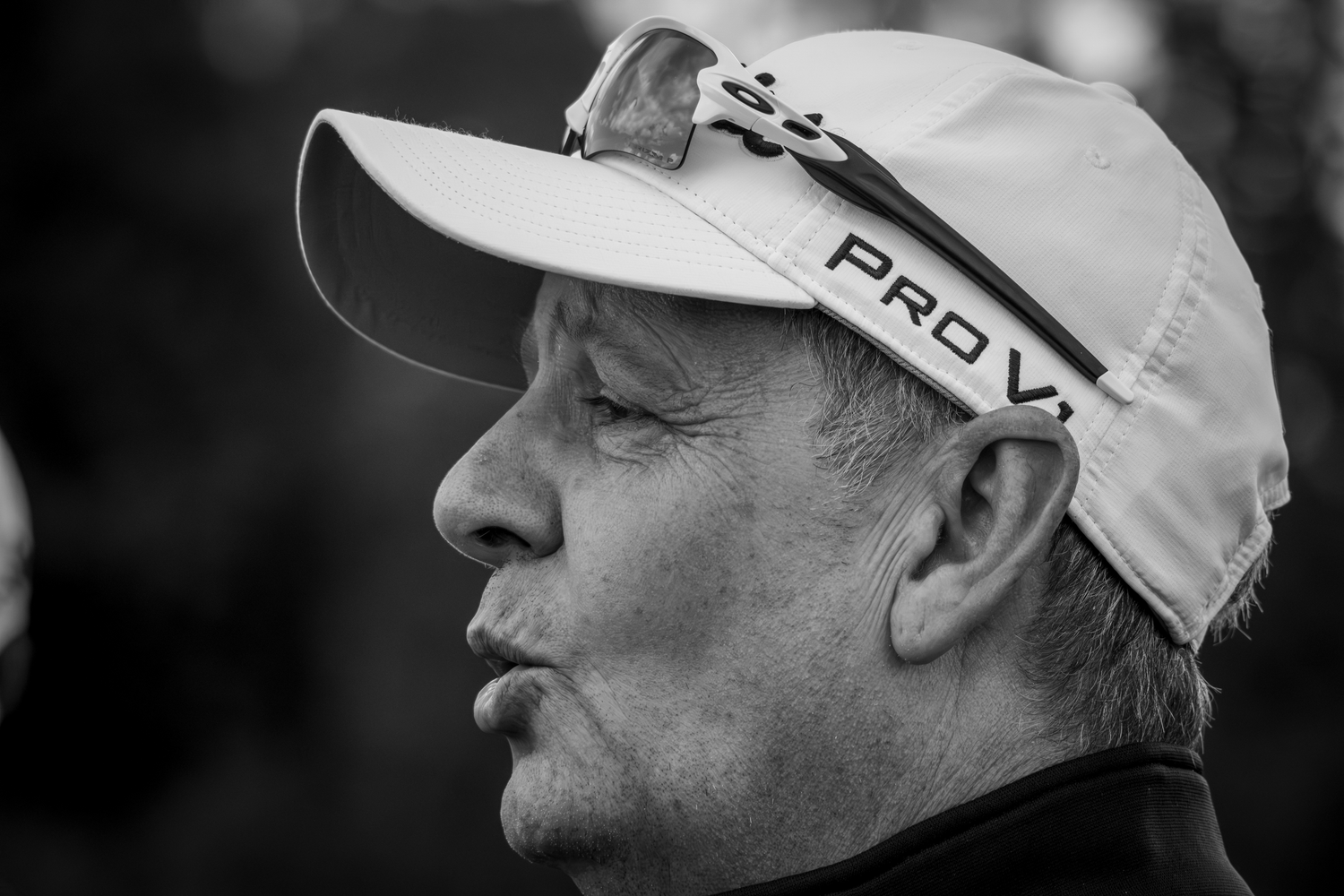 Black and white close-up profile of an older man wearing a white Pro V1 golf cap.