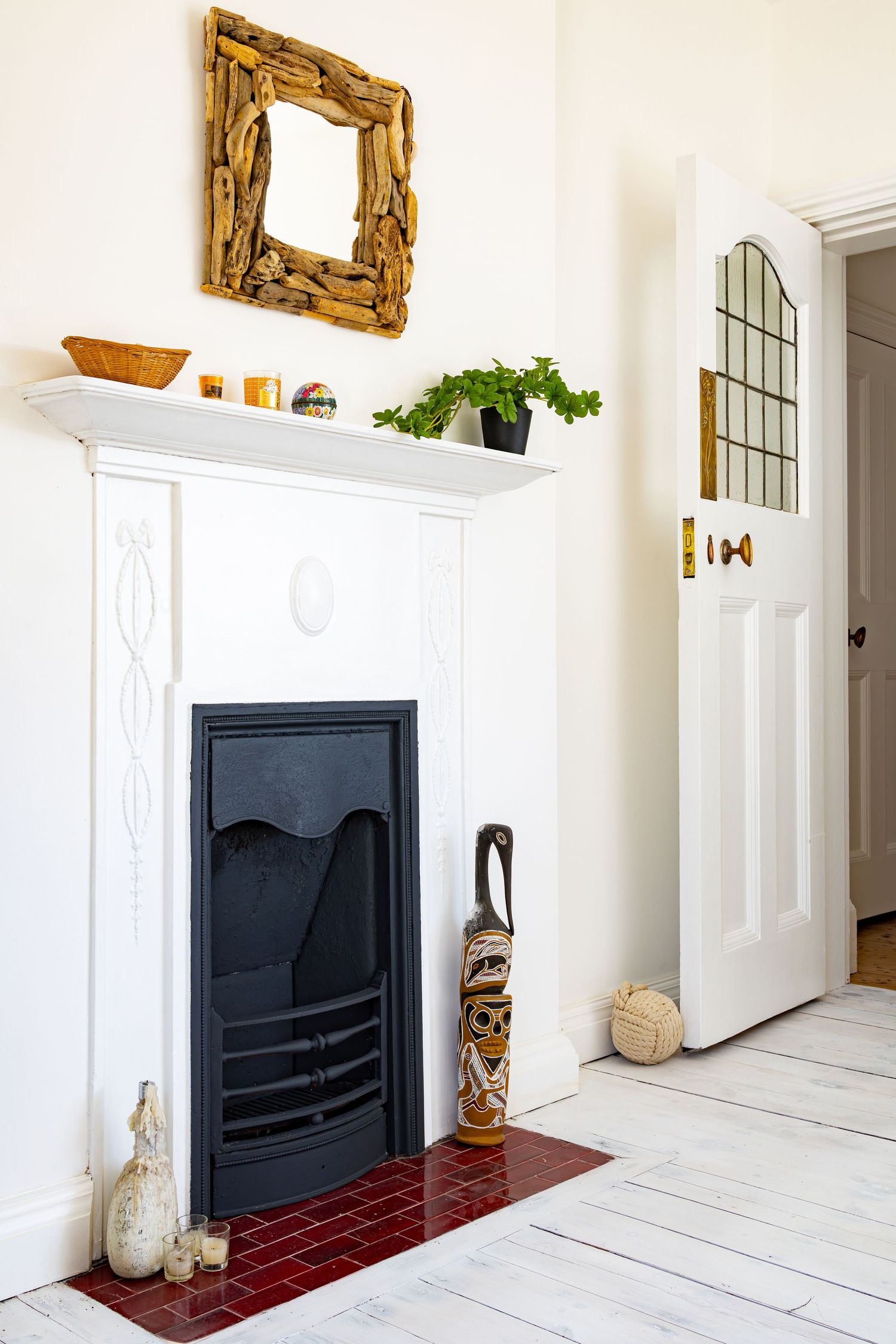 White Victorian fireplace with black cast iron insert, driftwood mirror and decorative tribal art piece.