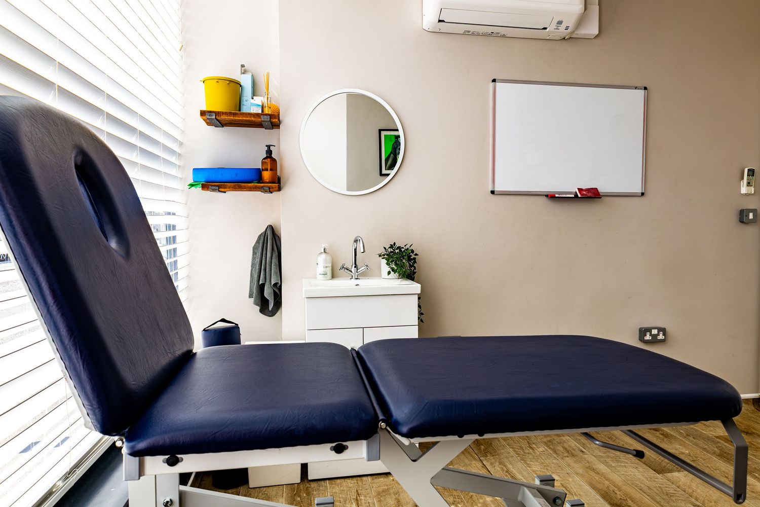 Clean therapy room with blue treatment table, round mirror, whiteboard, and shelving with supplies.