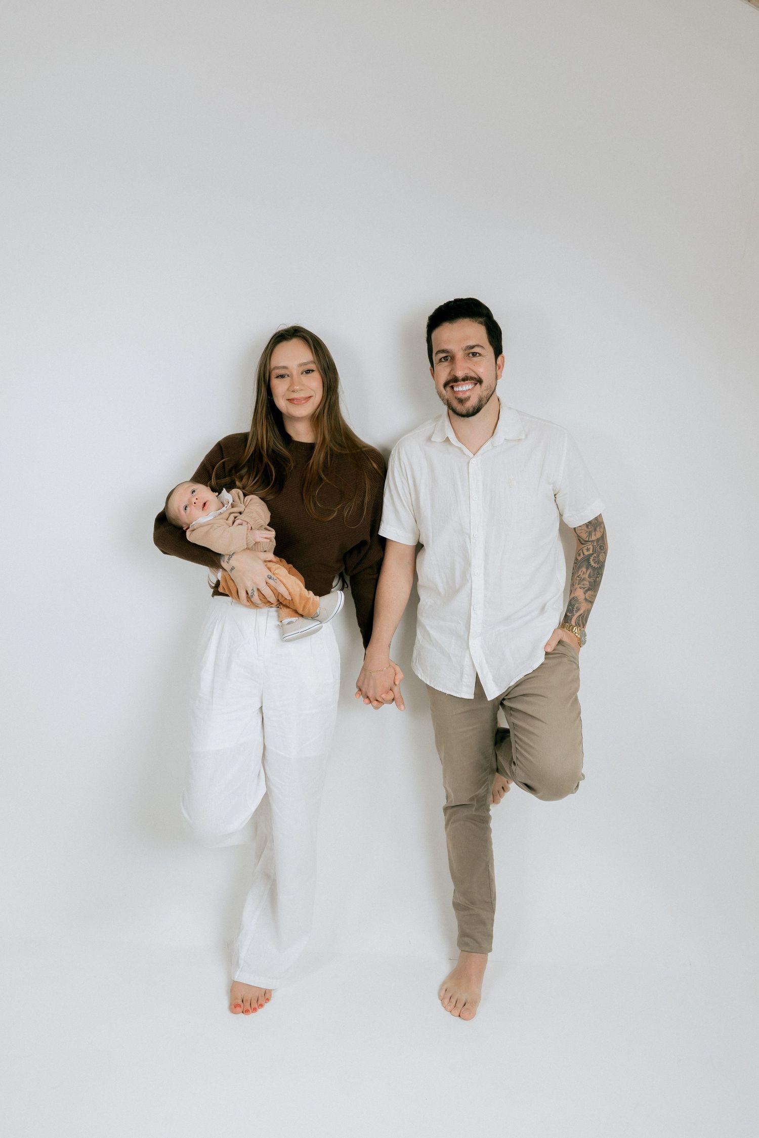 Young family with baby posing together against a white studio background.