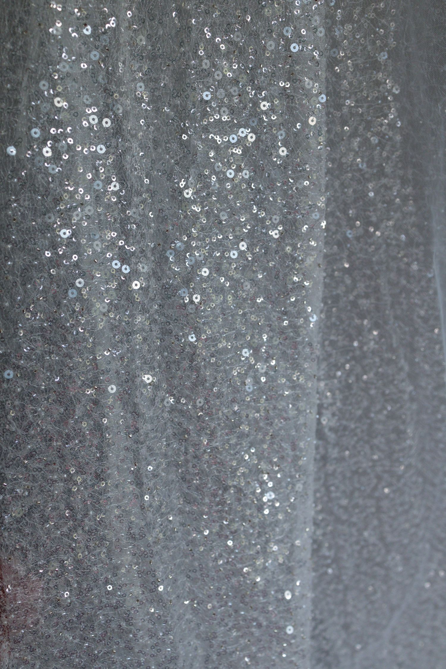 Silver sequin fabric texture with shimmering metallic embellishments creating an elegant glittery background.