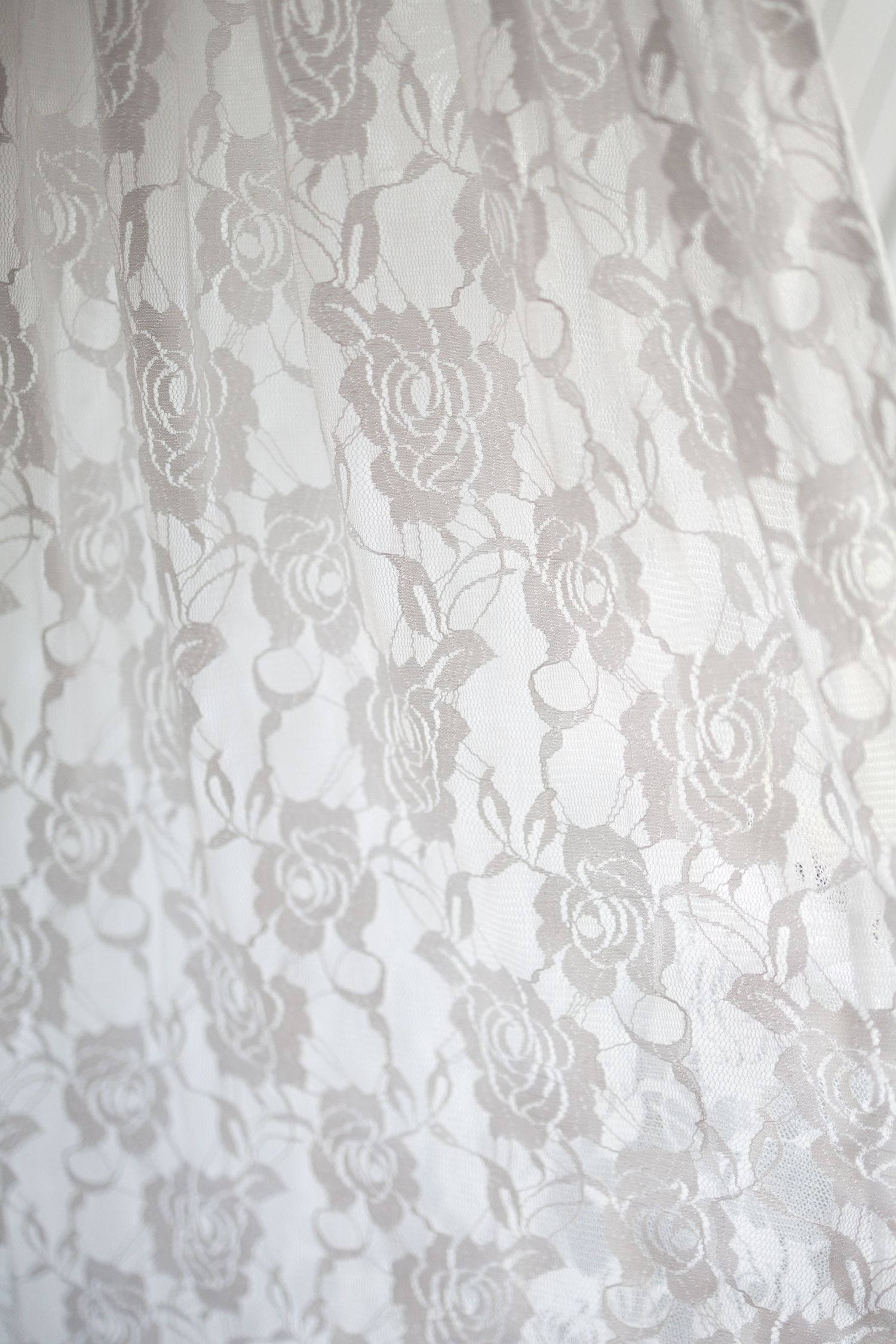 White lace fabric with delicate rose floral pattern, soft diffused light creating elegant texture detail.