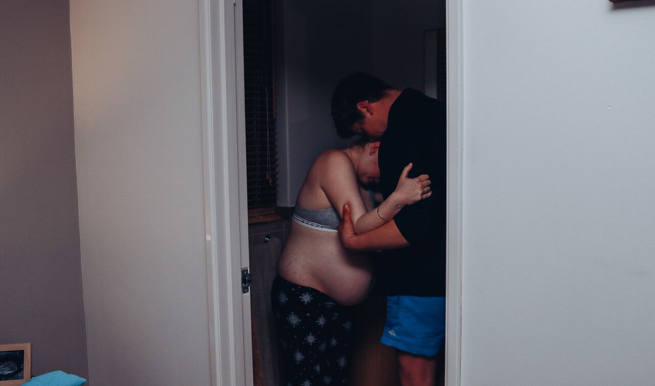 Couple sharing an intimate embrace in a doorway, captured in a candid lifestyle photography moment.