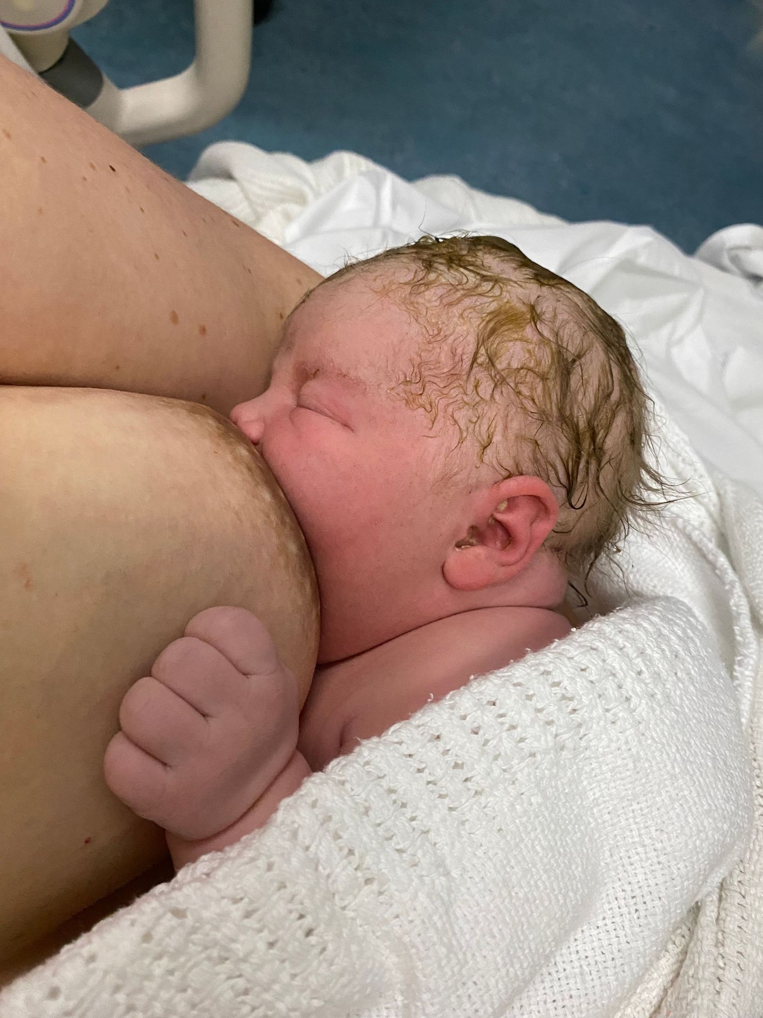 Newborn baby with wet hair breastfeeding for the first time shortly after birth in hospital.