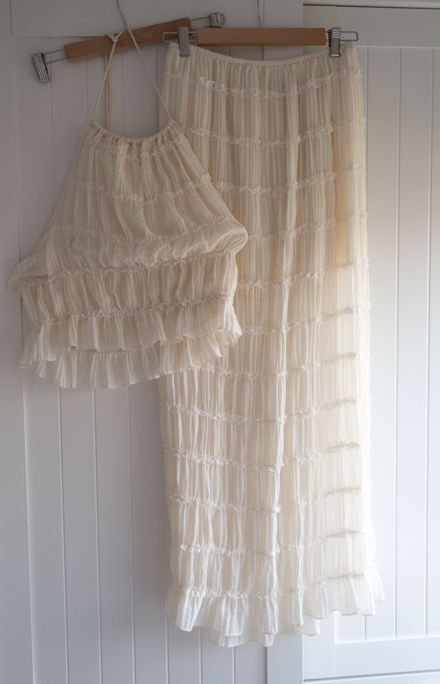 Cream ruffled two-piece set with tiered crop top and maxi skirt, displayed on a wooden hanger.