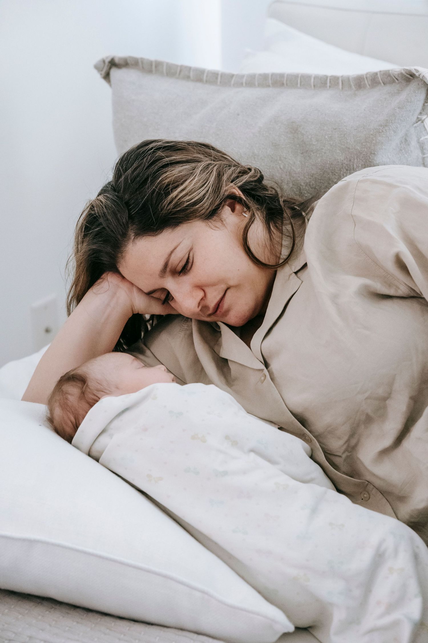 New mother lying in bed gazing lovingly at her sleeping newborn baby.