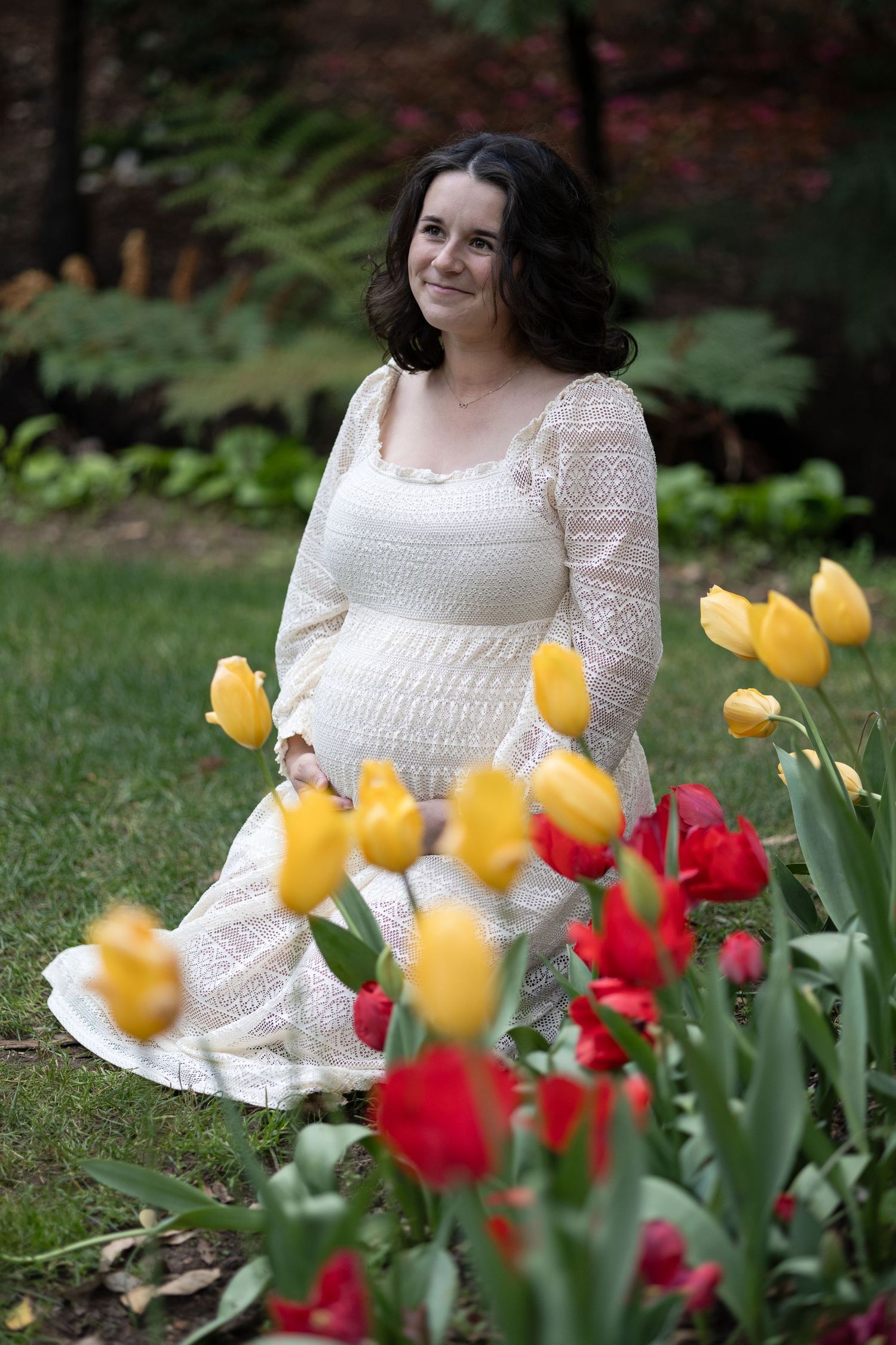 Pregnant woman in white lace dress kneeling among colorful tulips in garden.  Araluen Perth